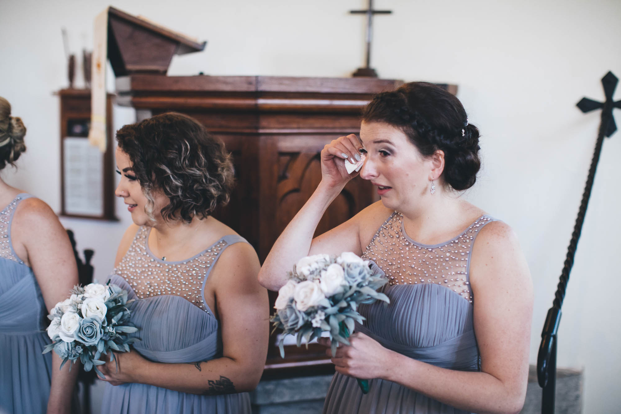 Bridesmaid wipes away tears as she sees her friend walk down the aisle in a church