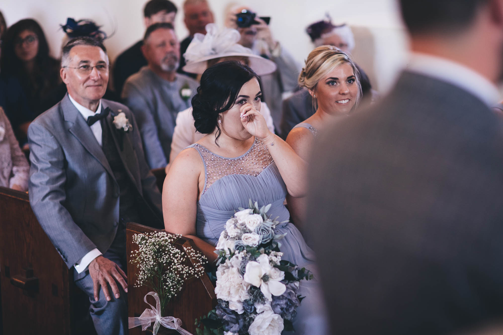 Bridesmaid wipes away a tear as she and other wedding guests watch the wedding ceremony