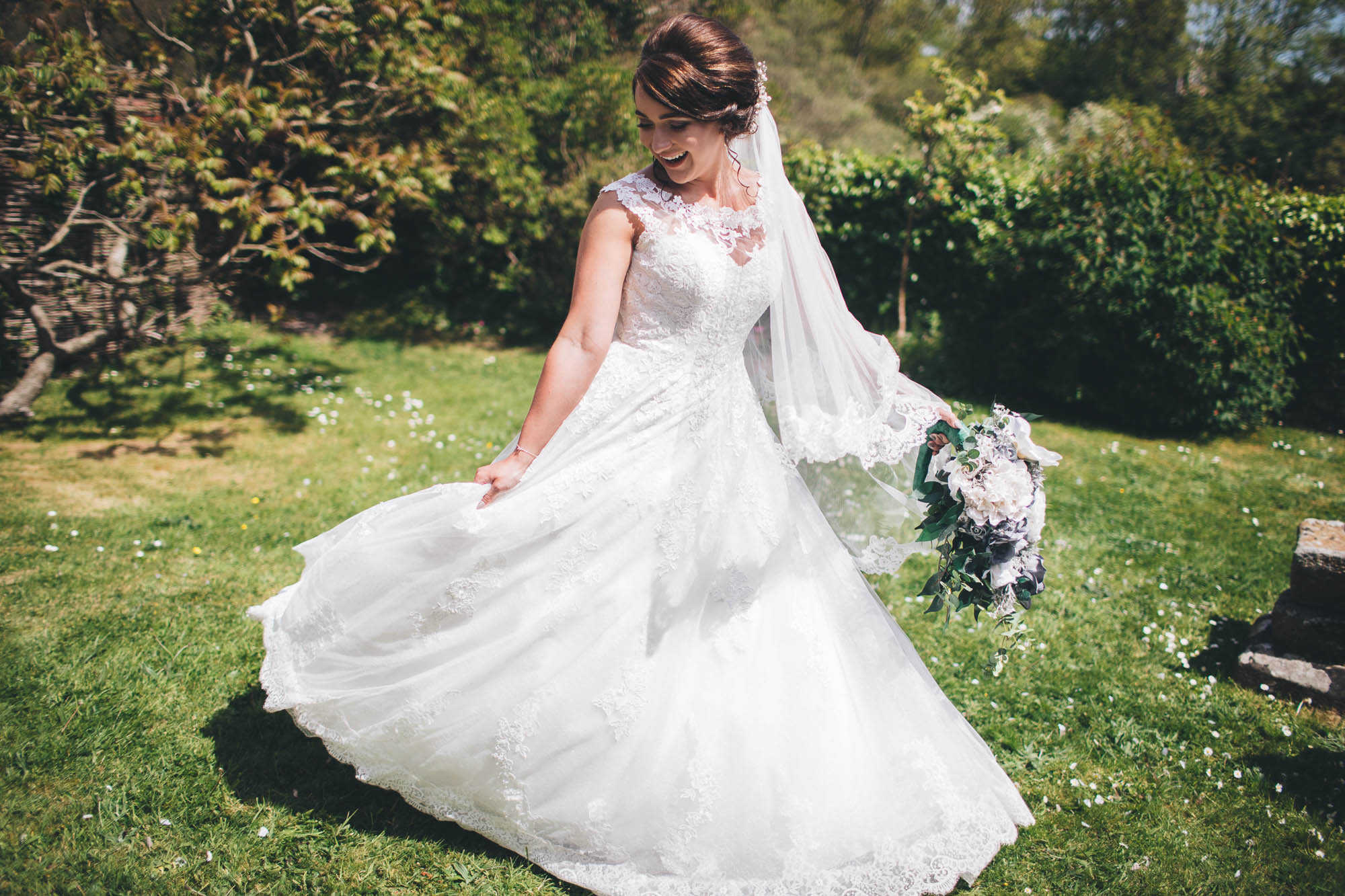 Blushing bride spins round in wedding dress on lush green grass