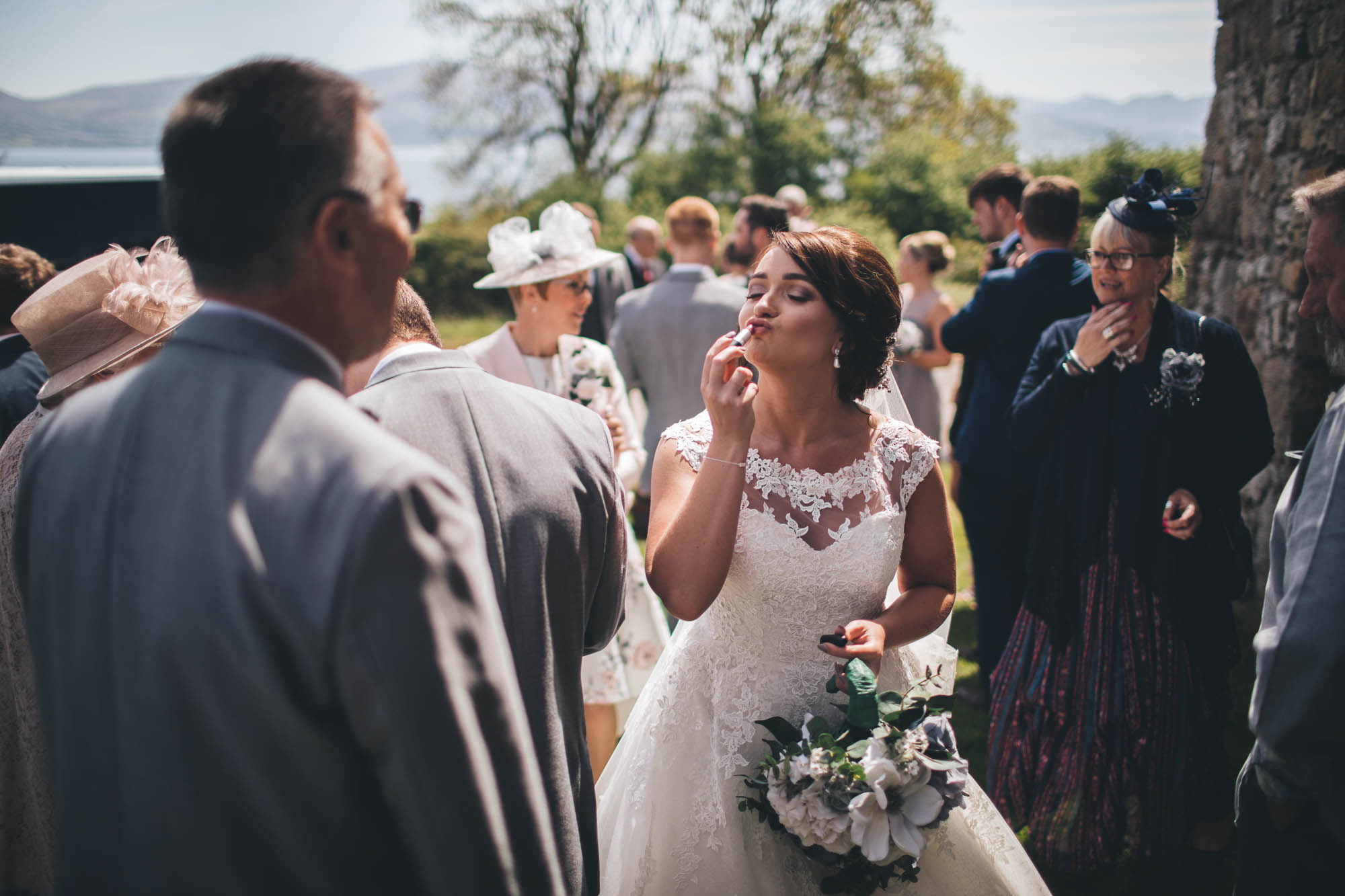 Bride pulls a funny face as she puts on her lipstick in front of her wedding guests just after the ceremony