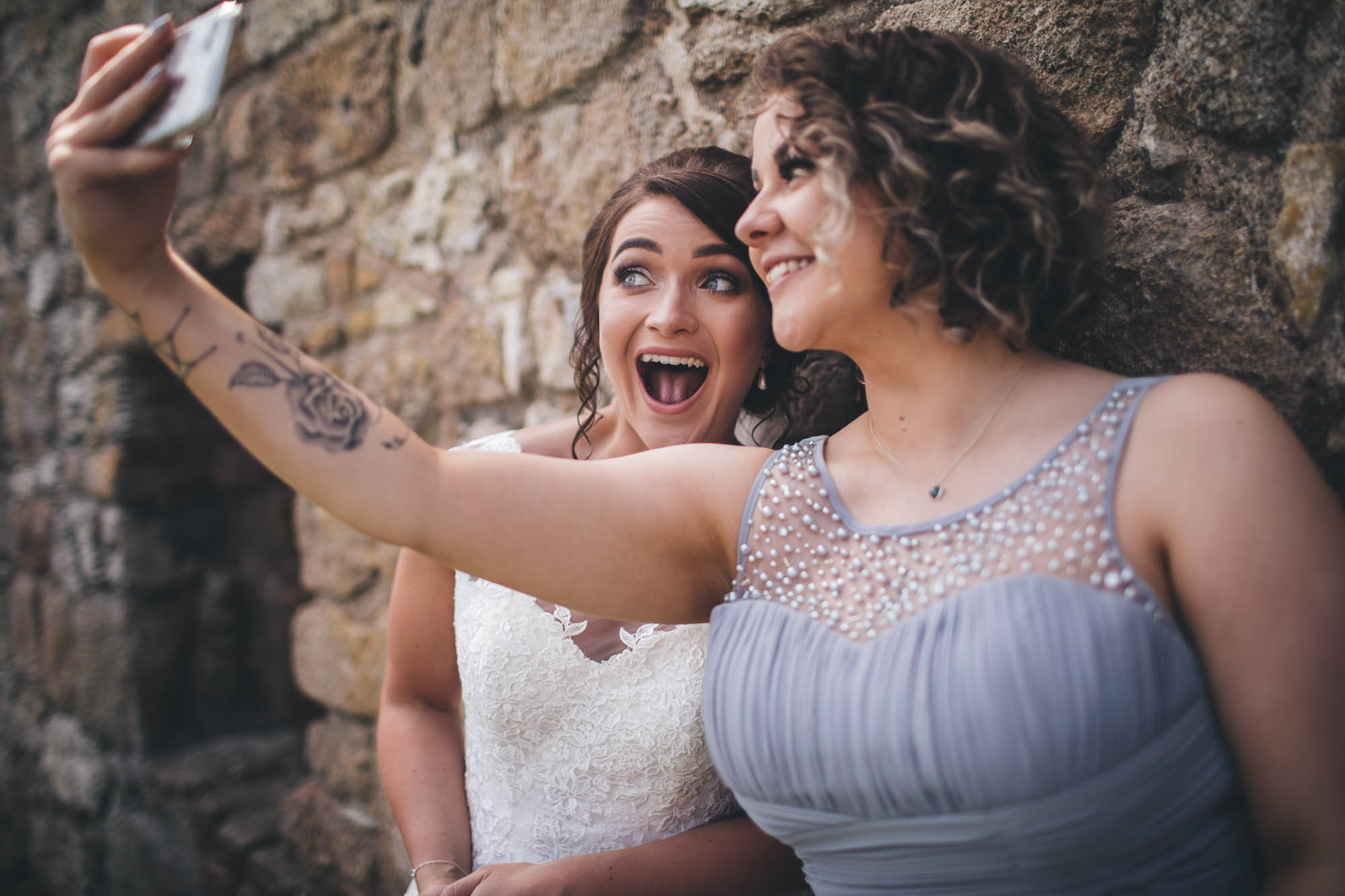 Bride and Bridesmaid take a cheeky selfie against stone brick wall