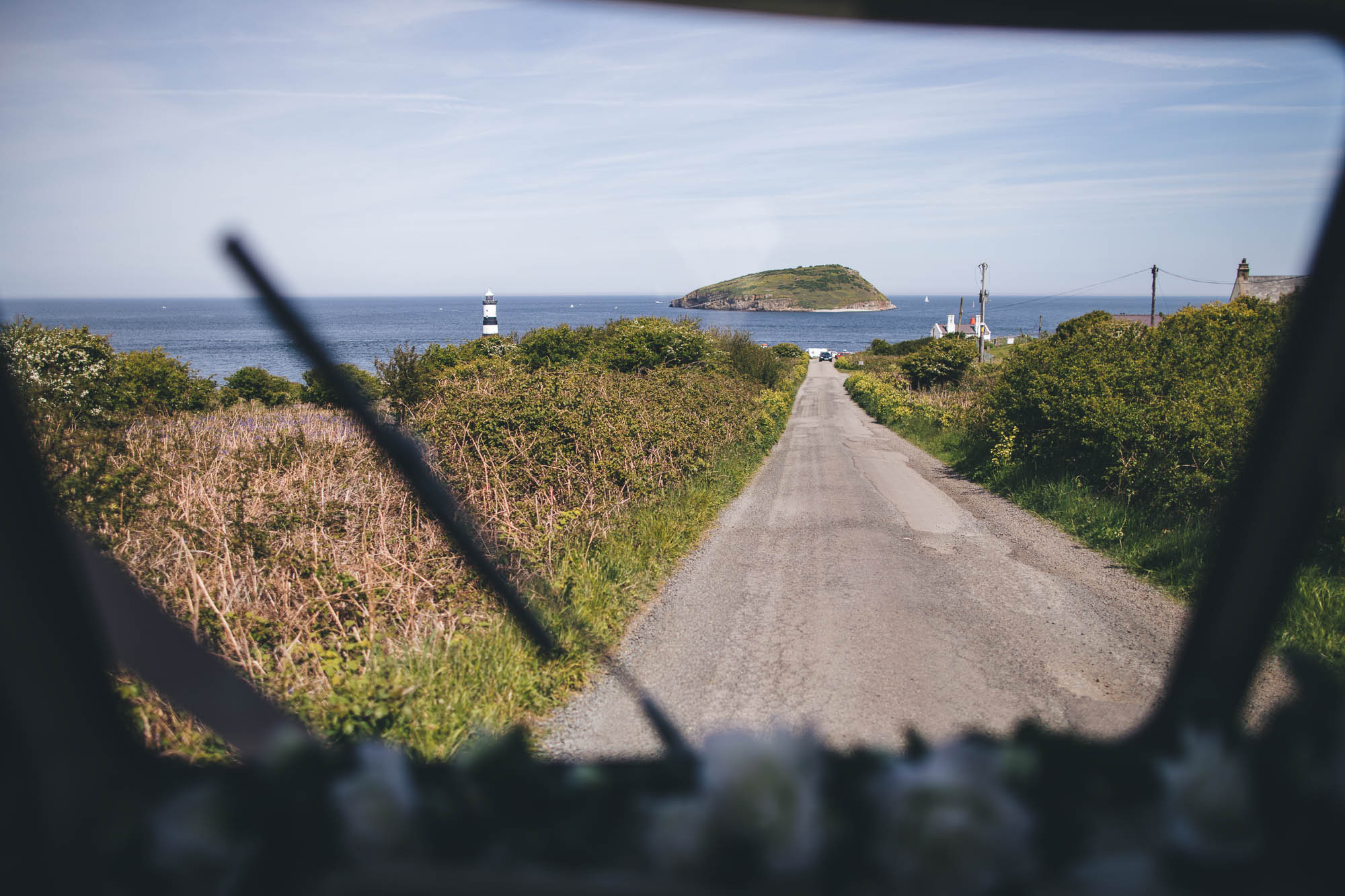 Looking down a country road through vintage car window to see the coastline and small Welsh island in the distance