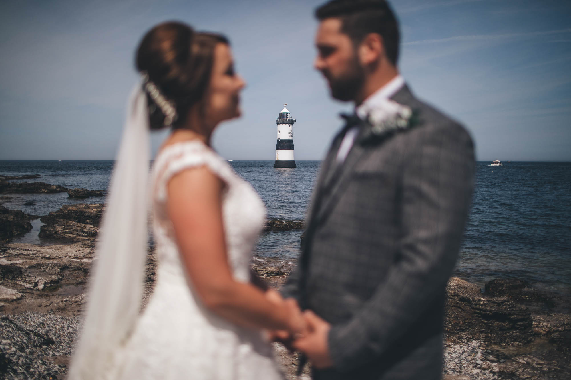 Bride and Groom are out of focus in the foreground looking lovingly at one another to draw attention to the lighthouse and coastline in the background
