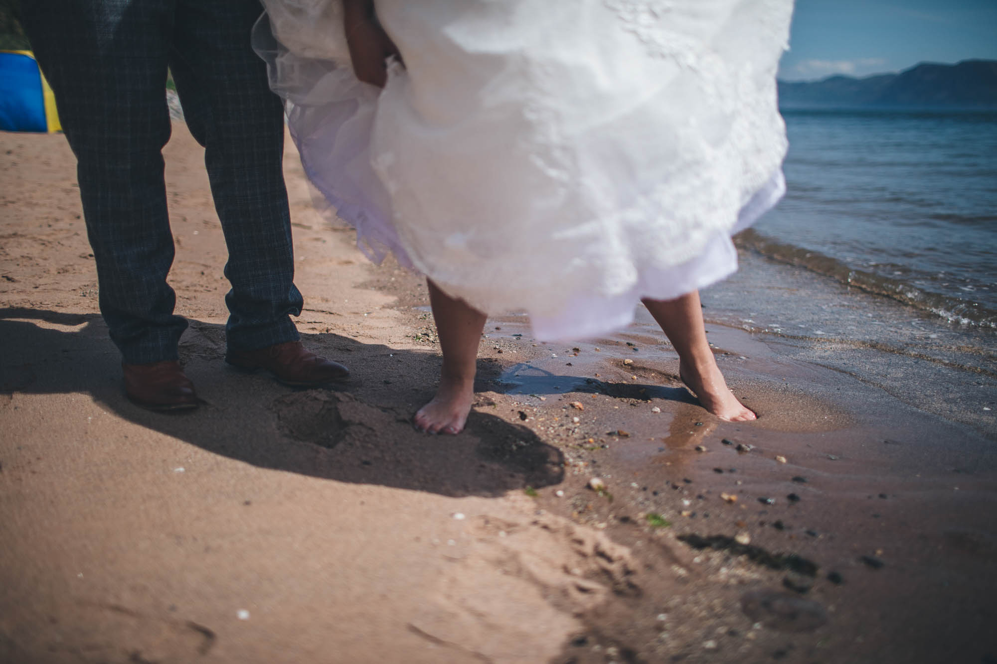 Low shot of Bride lifting her wedding dress as she steps out of the seaside after a quick paddle