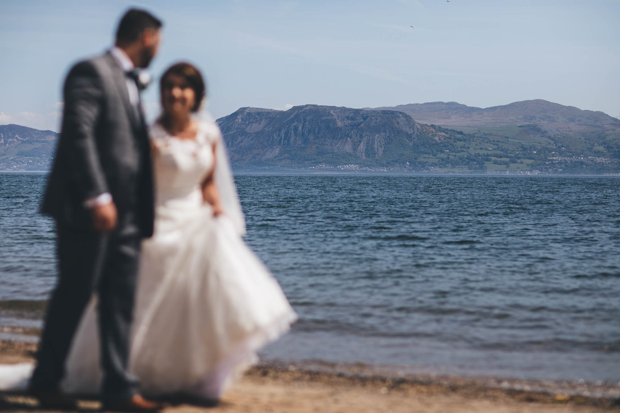 The bride and groom are out of focus in the foreground of the shot to draw the attention to the snowdonia mountainscape and sea in the background