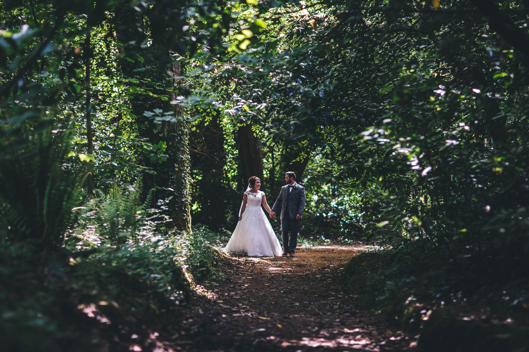 Vivid green shot of just married couple in the distance walking through trees and woodland