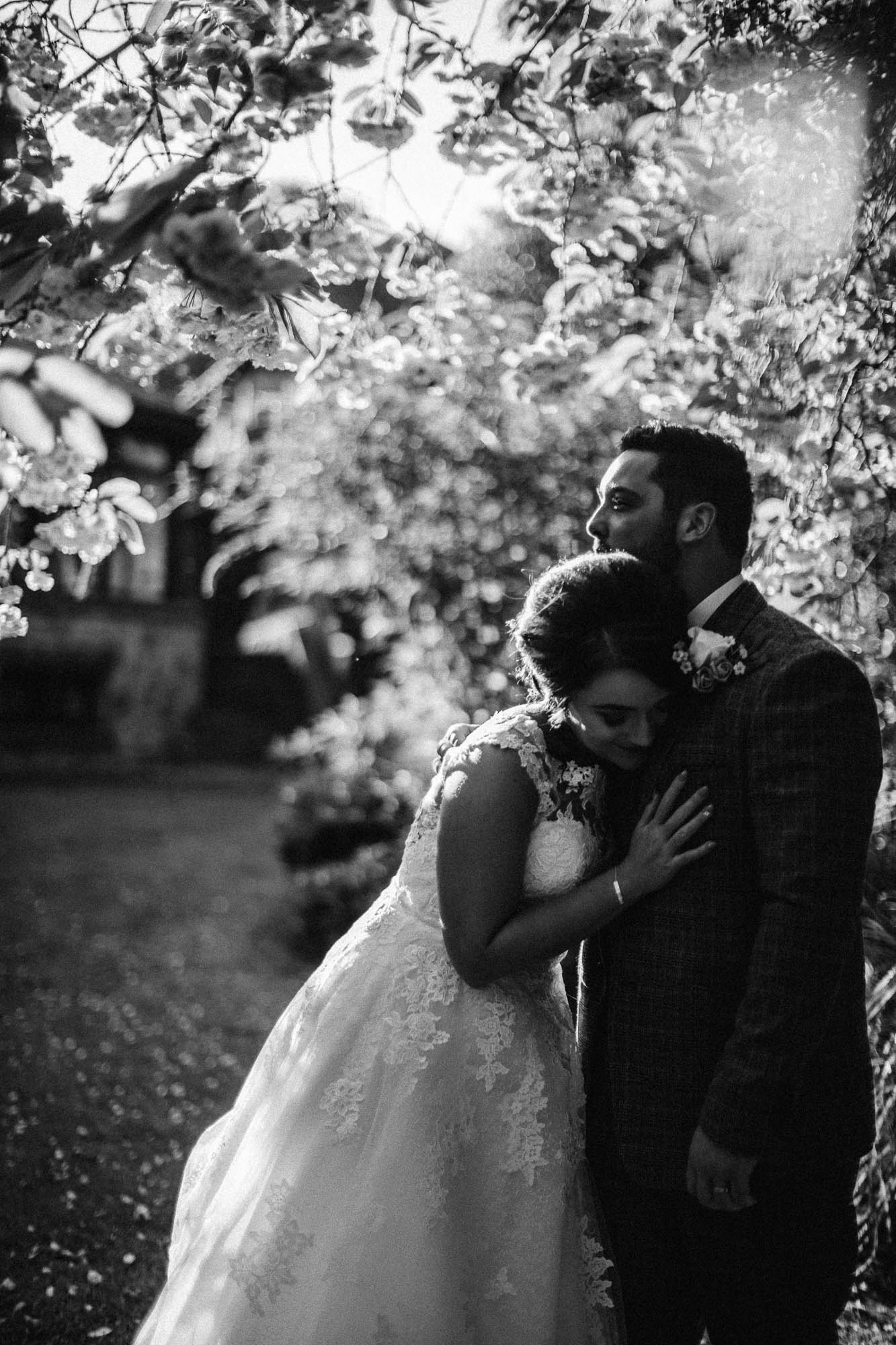 Black and white shot of bride lovingly leaning on Groom in Wedding Garden