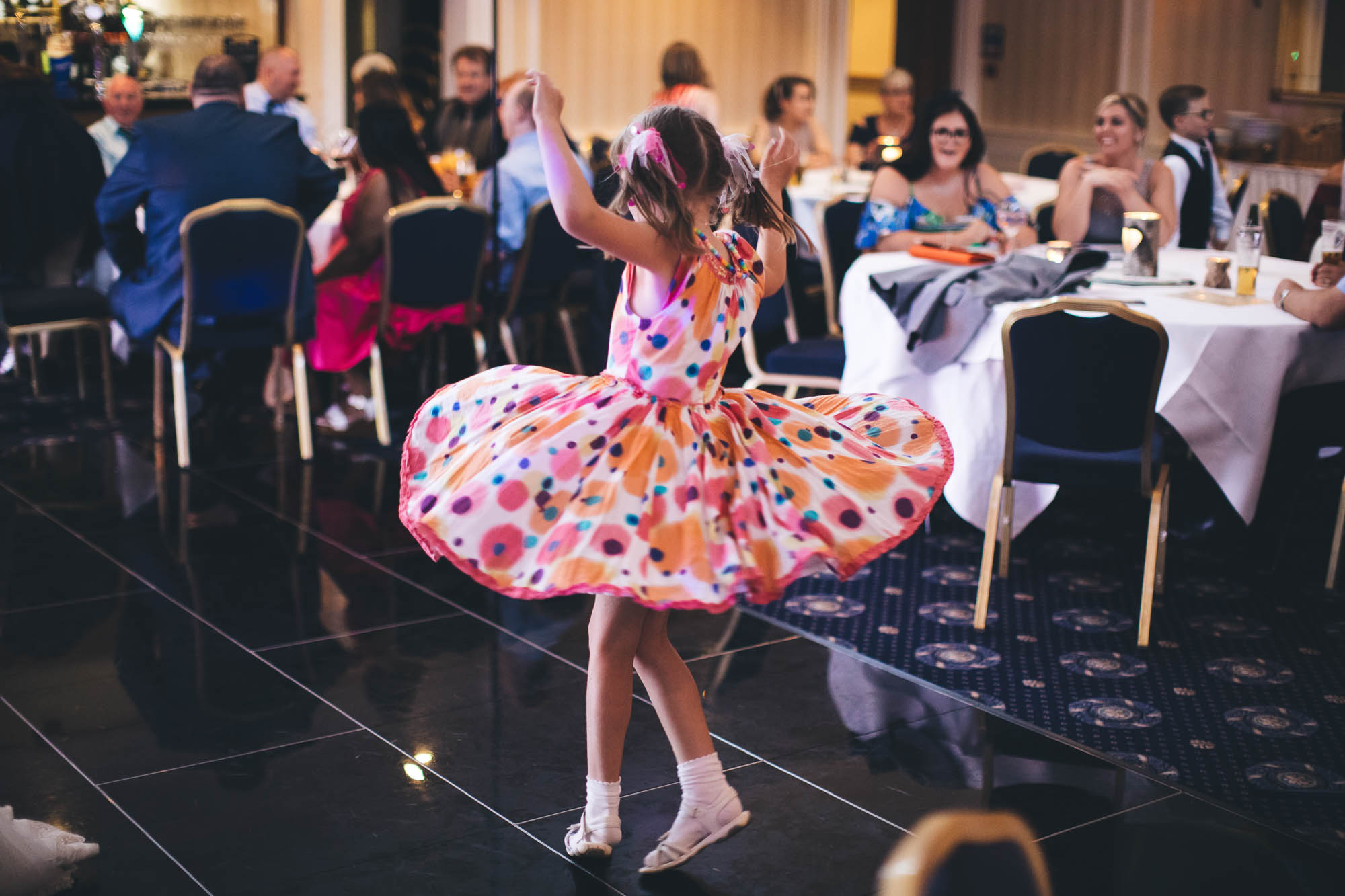 Young girl spins round on dance floor showing off her colourful dress at wedding reception