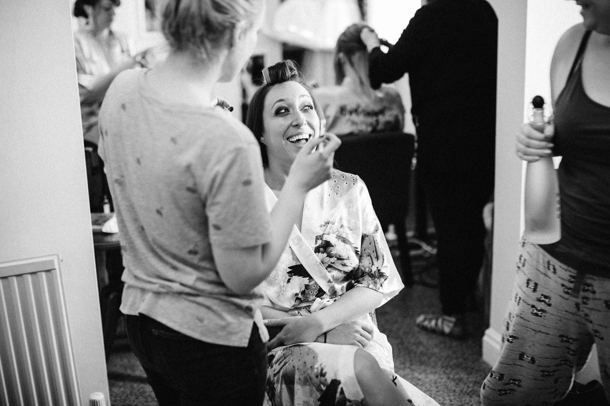 Bride laughing with friend whilst getting her make up done