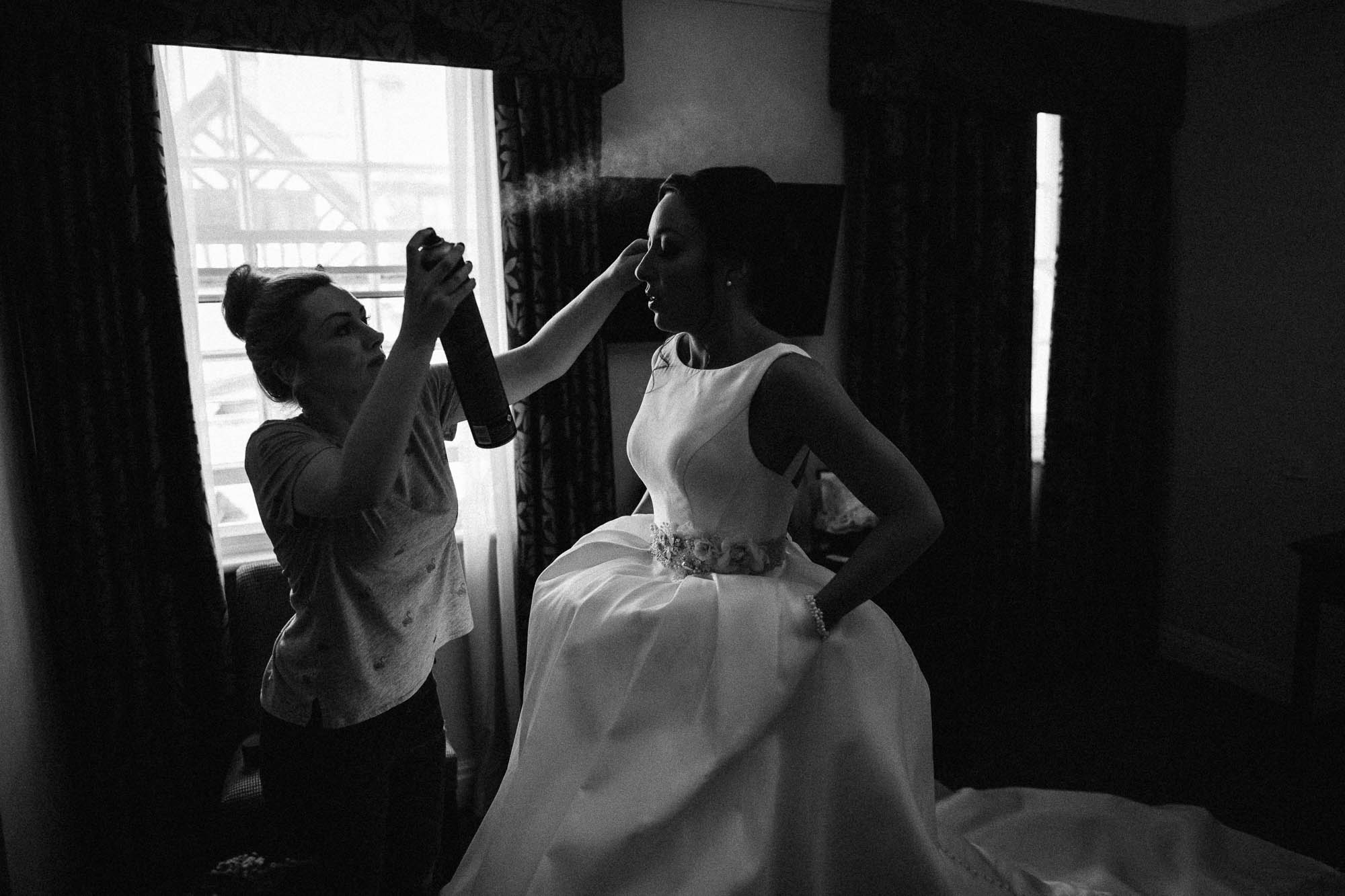 Bride getting ready with wedding dress on and stylist doing finishing touches