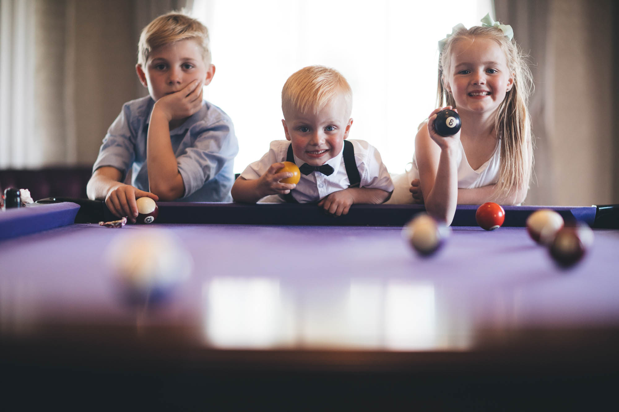 Children smile for the camera at wedding holding pool balls