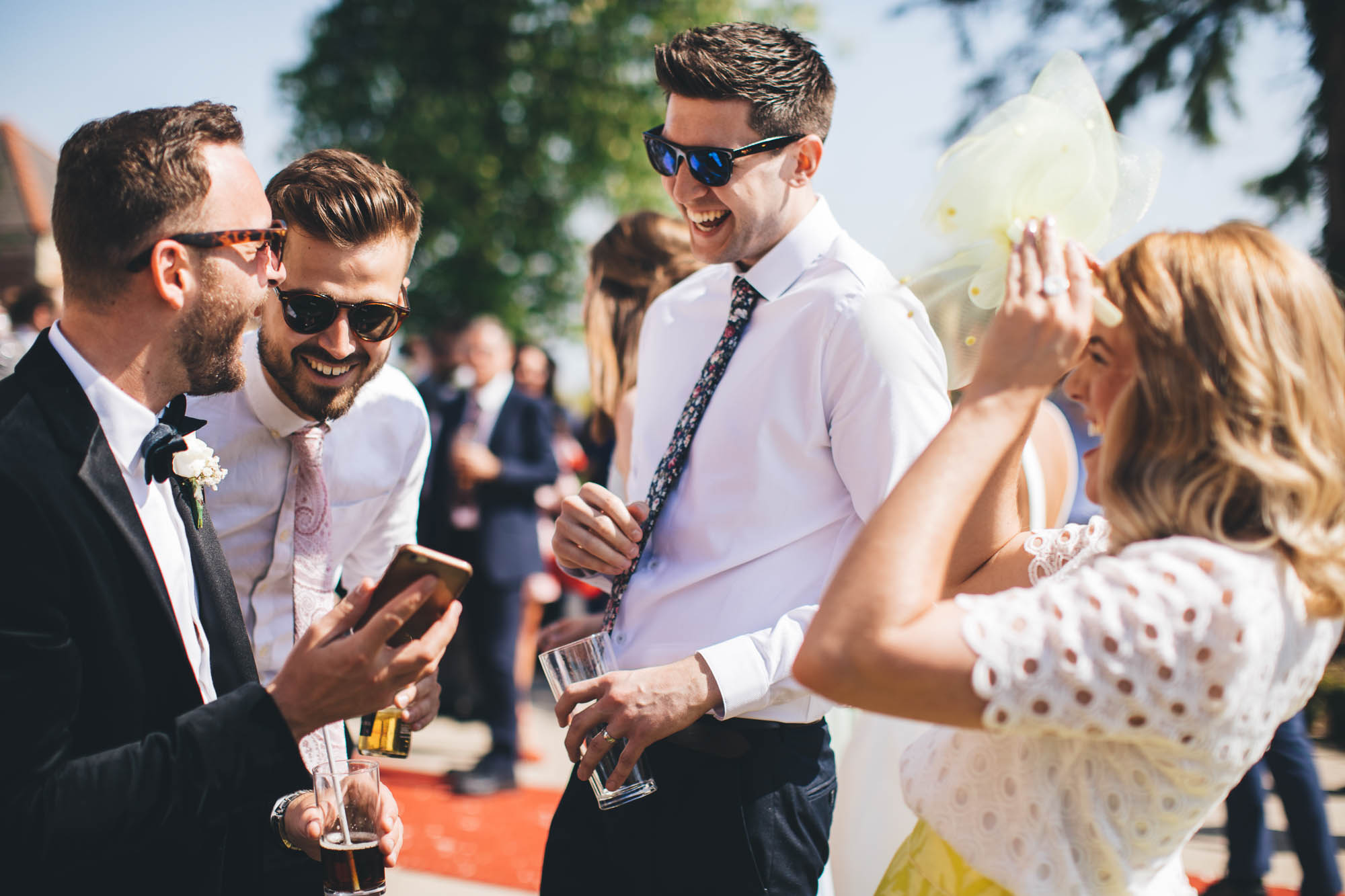 Groom shows wedding guests something funny on his phone that everyone laughs at