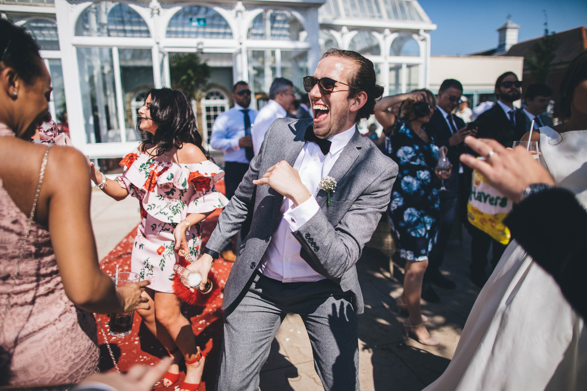 Groomsman dances with other guests outside wedding venue