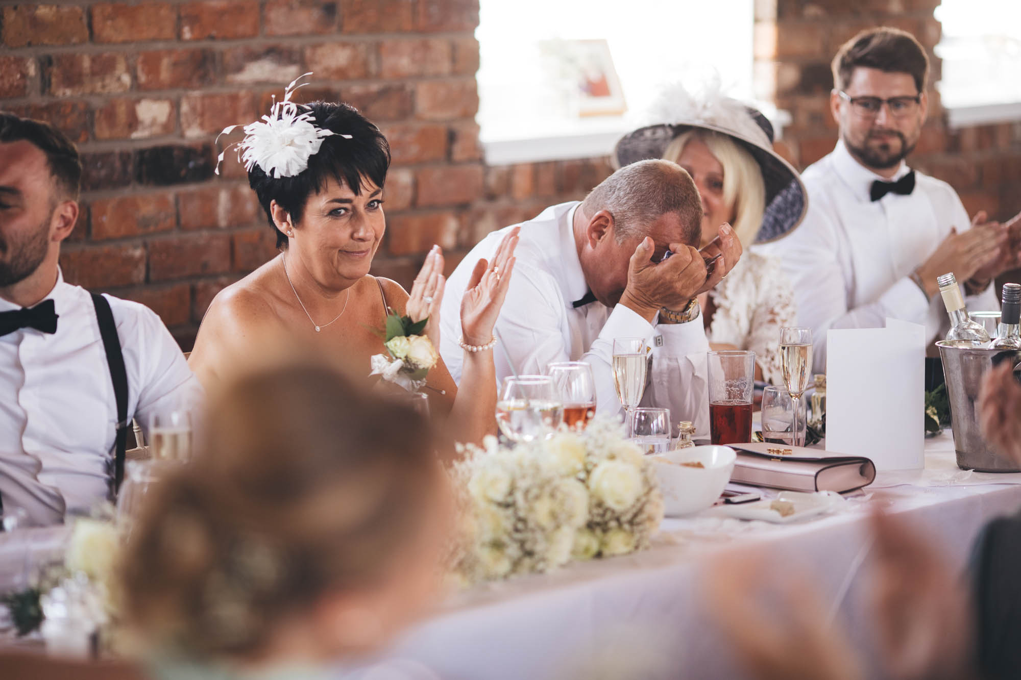 Mother of the Groom knowingly look at wedding guests and applaud whilst Father of the Groom wipes his tears