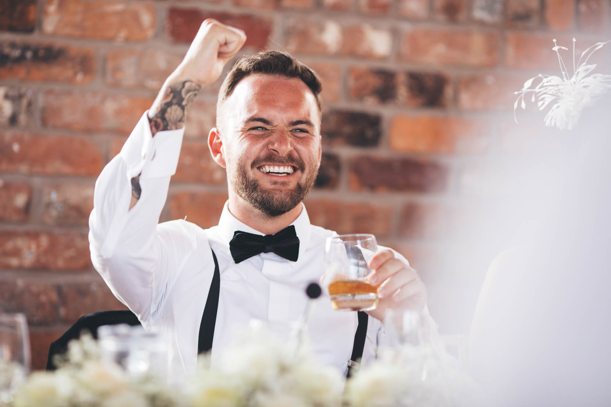 Groom punches the air at the top table whilst holding his drink