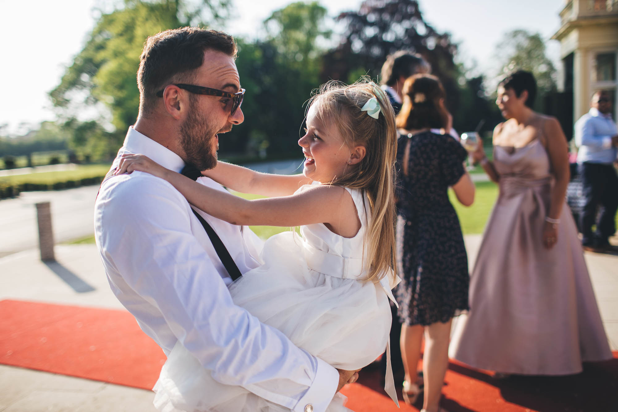 Groom picks up flower girl and makes her laugh outside wedding venue as sun is going down