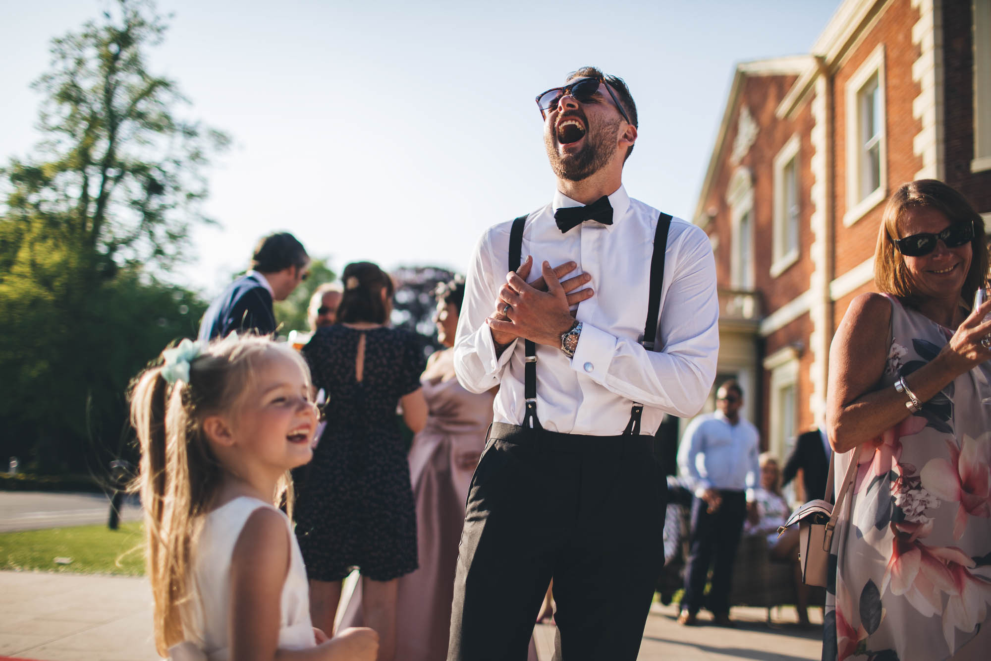 Groom wears sunglasses and laughs at something hilarious outside wedding venue