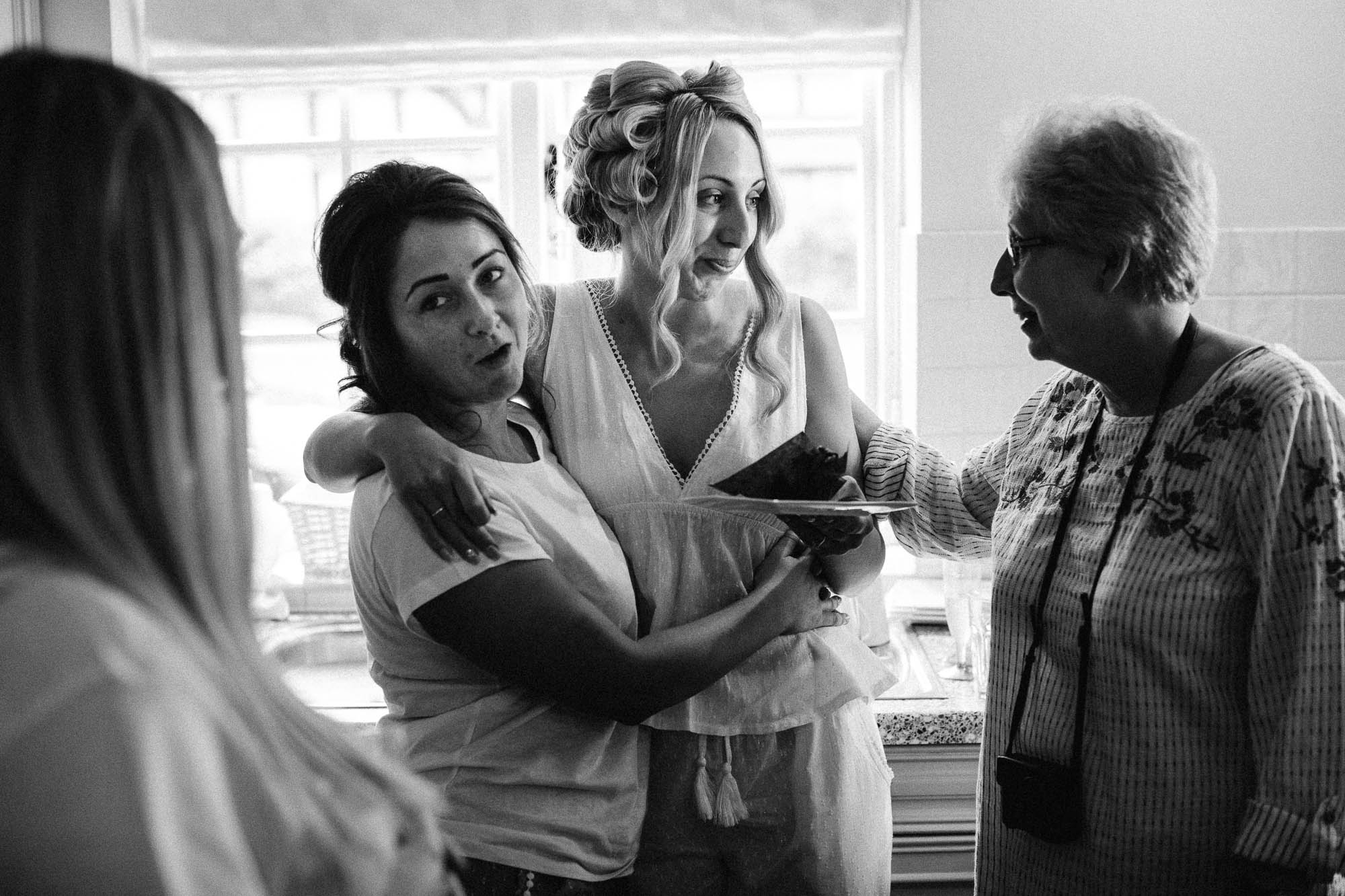 Black and white shot of bridal party chatting and eating cake whilst getting ready