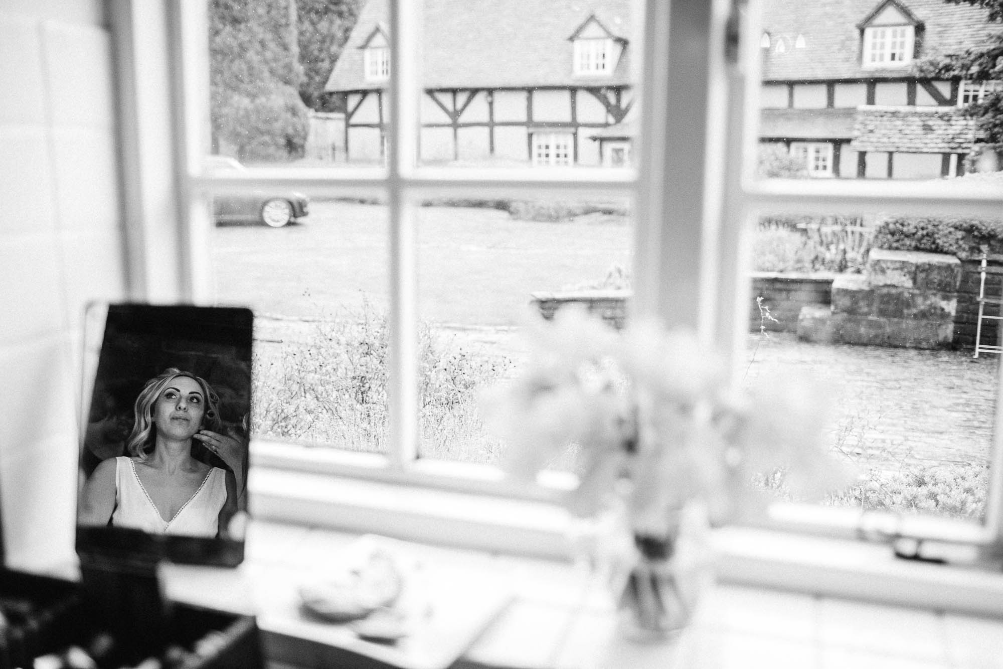 Reflection of bride getting make up done in black and white with The Granary at Dovehouse Farm in the background