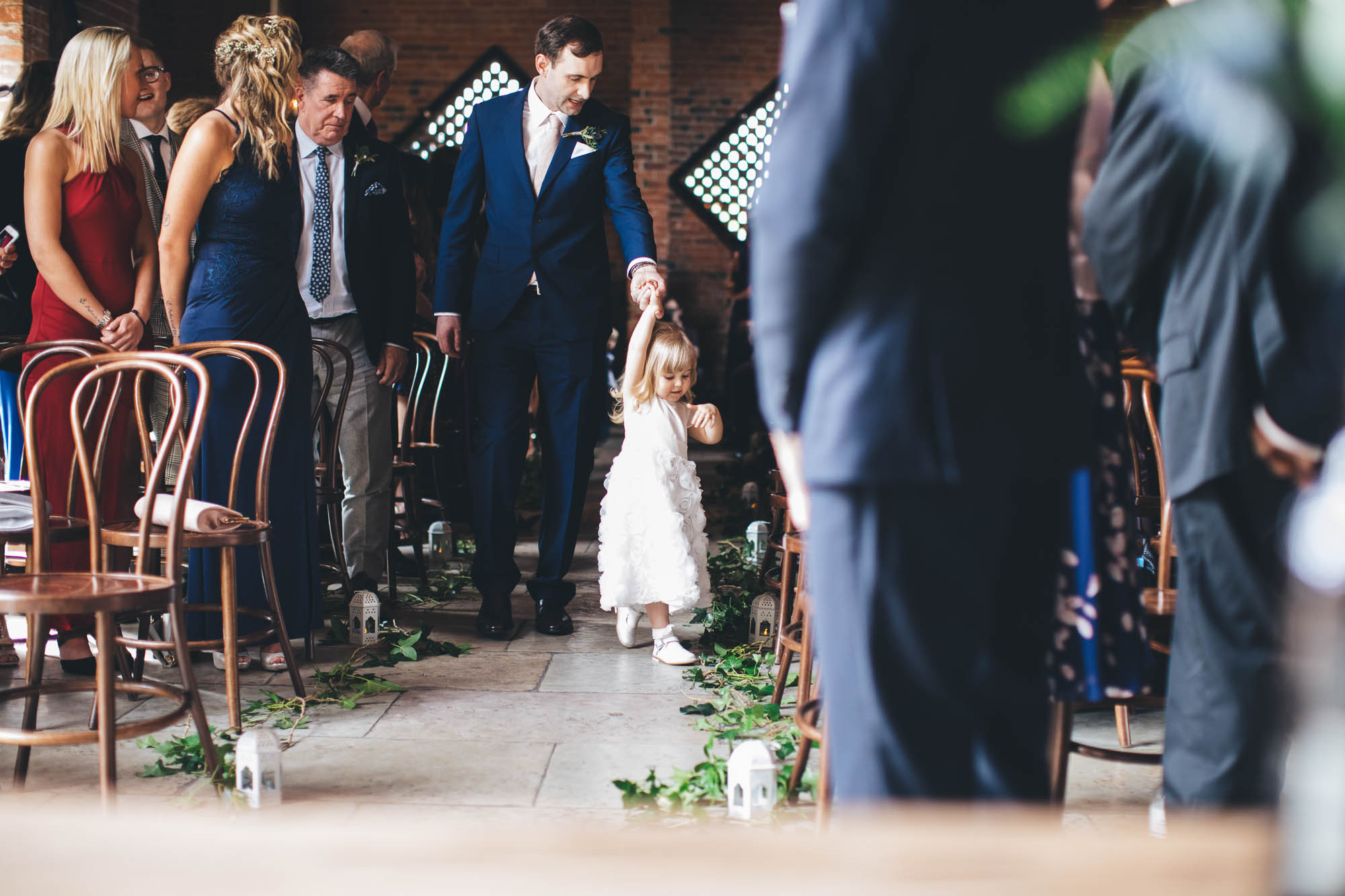 Wedding guest leads young girl down the aisle and wedding guests look on from their seats