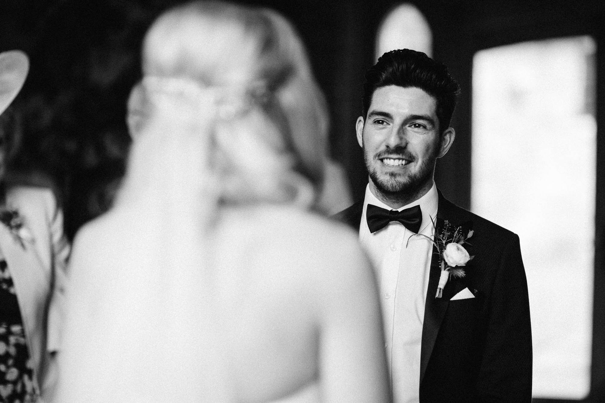 Black and white shot of groom smiling as he gets married