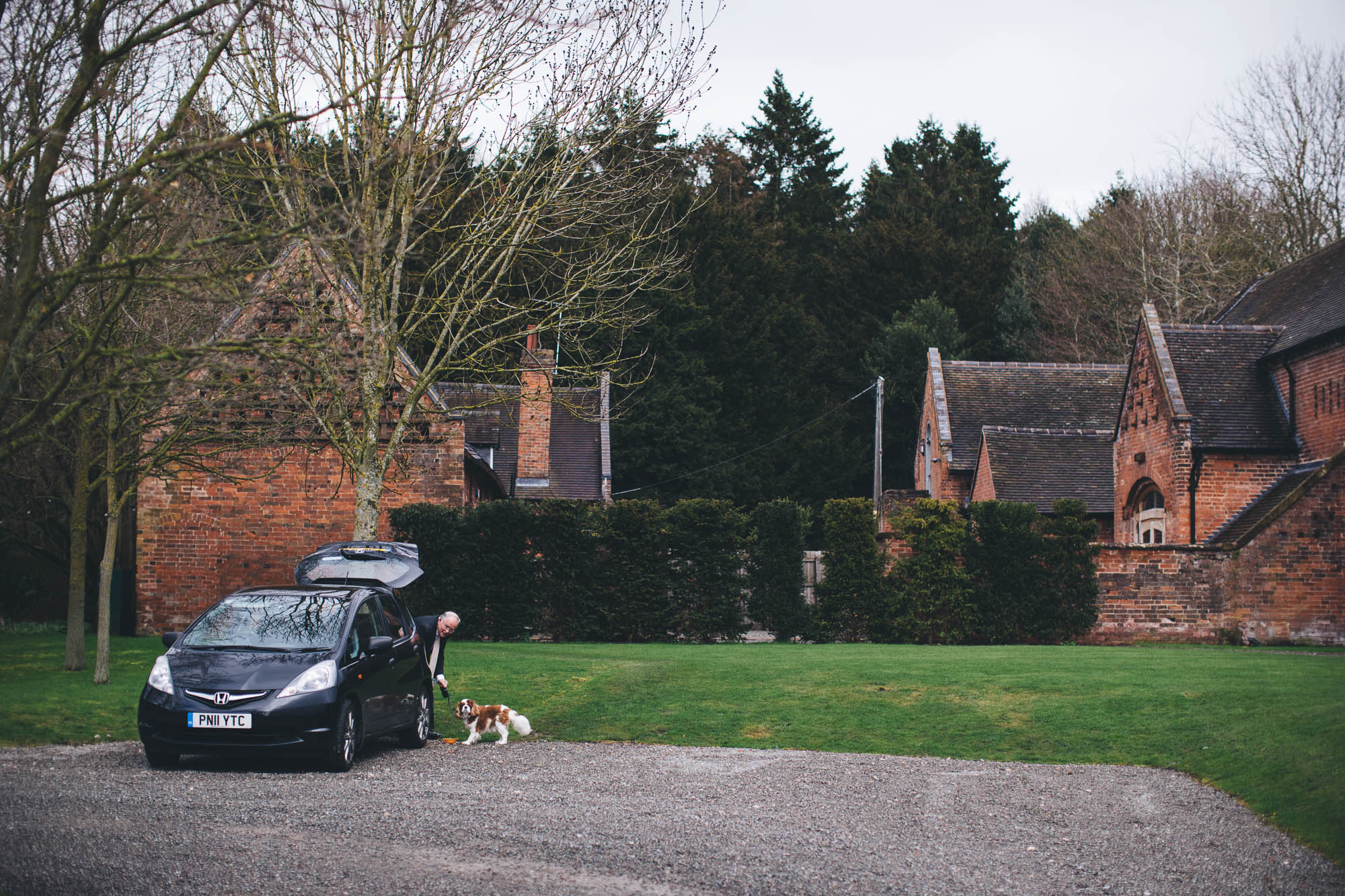Man attends to cute dog by his car outside rustic red brick barn