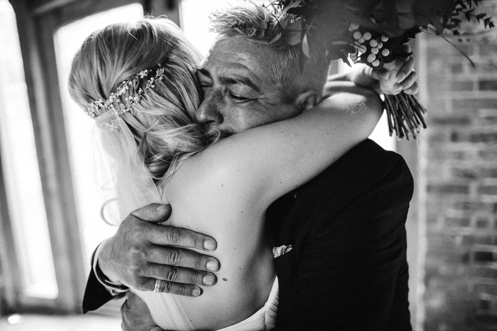Black and white shot of father embracing bride after the wedding