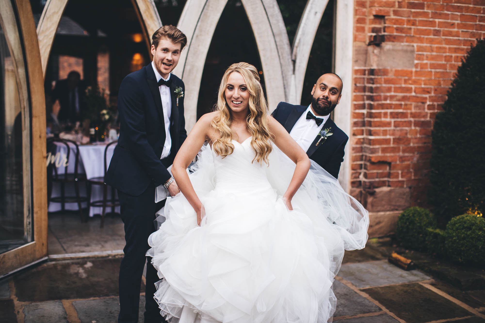 Groomsmen have banter as they help Bride with her wedding dress outside