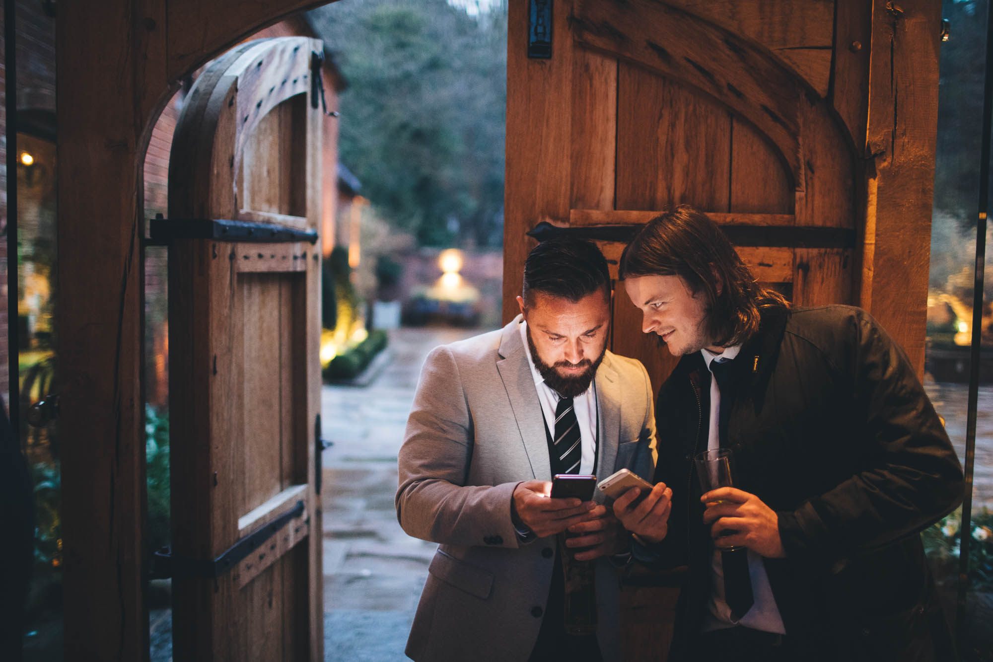 Wedding guests show each other photos on phone in rustic wooden doorway