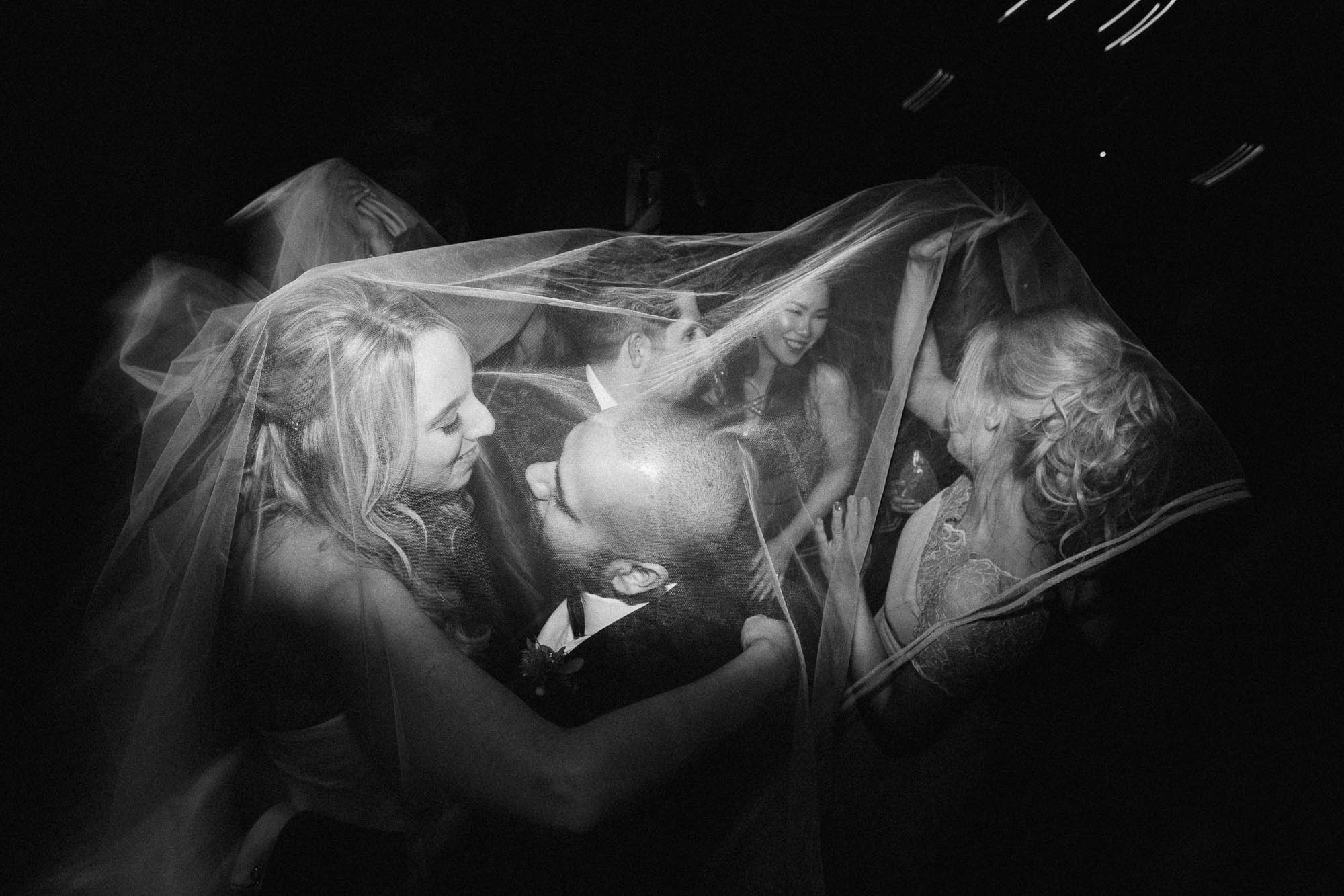 Bride, Groom and wedding guests dance under bridal veil on dance floor