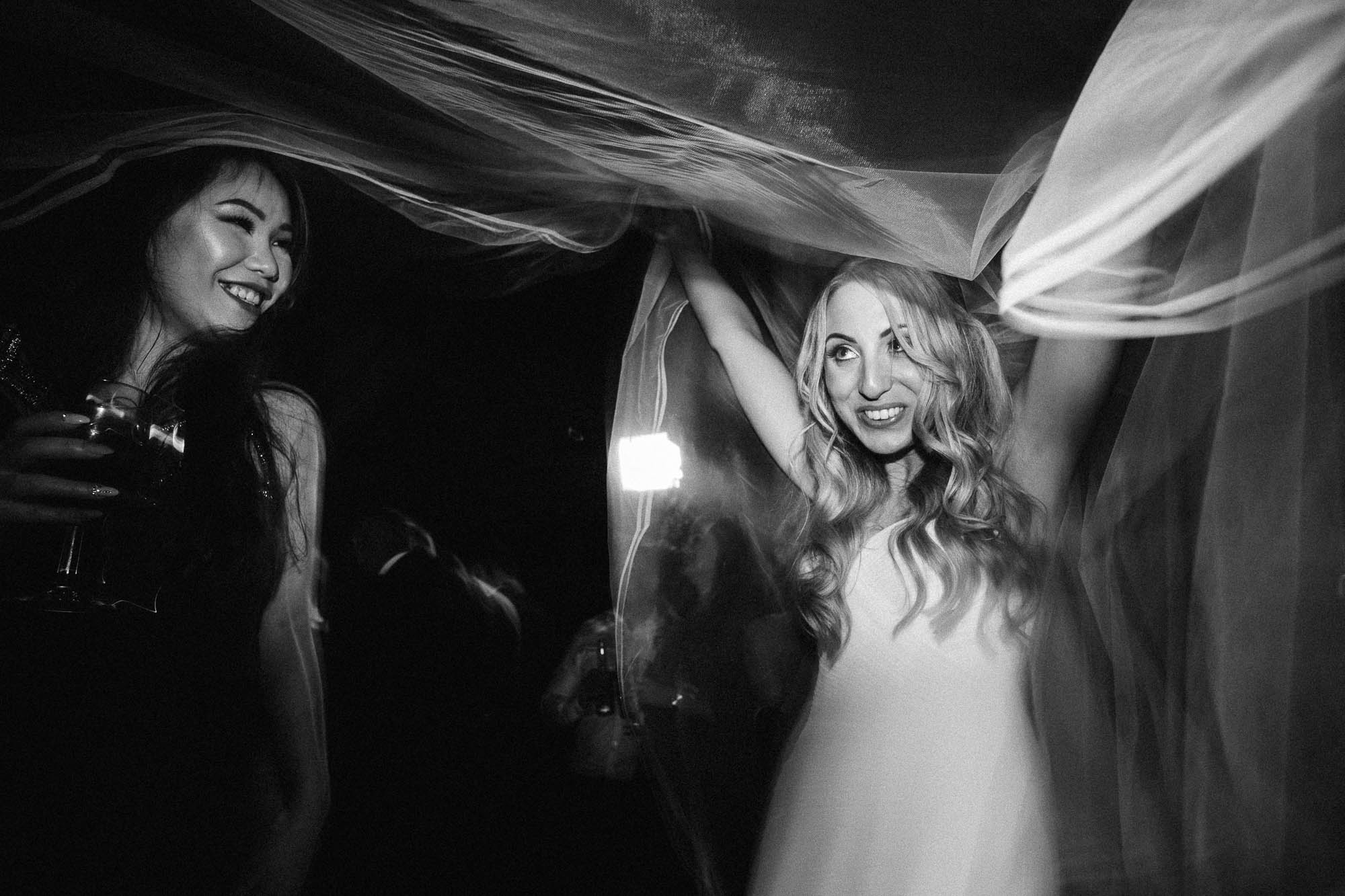Bride looks coy in black and white as she lifts veil on dancefloor