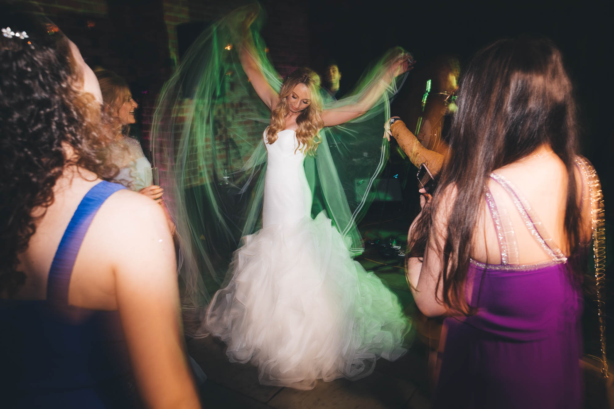 Bride plays with dress as she dances on dancefloor while guests watch