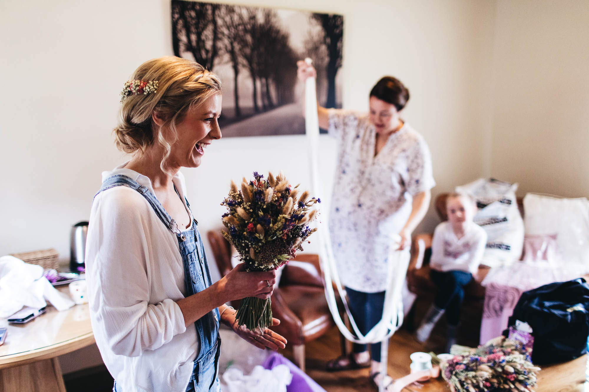 Bride holds wedding bouquet at wedding preparations while family helps in background