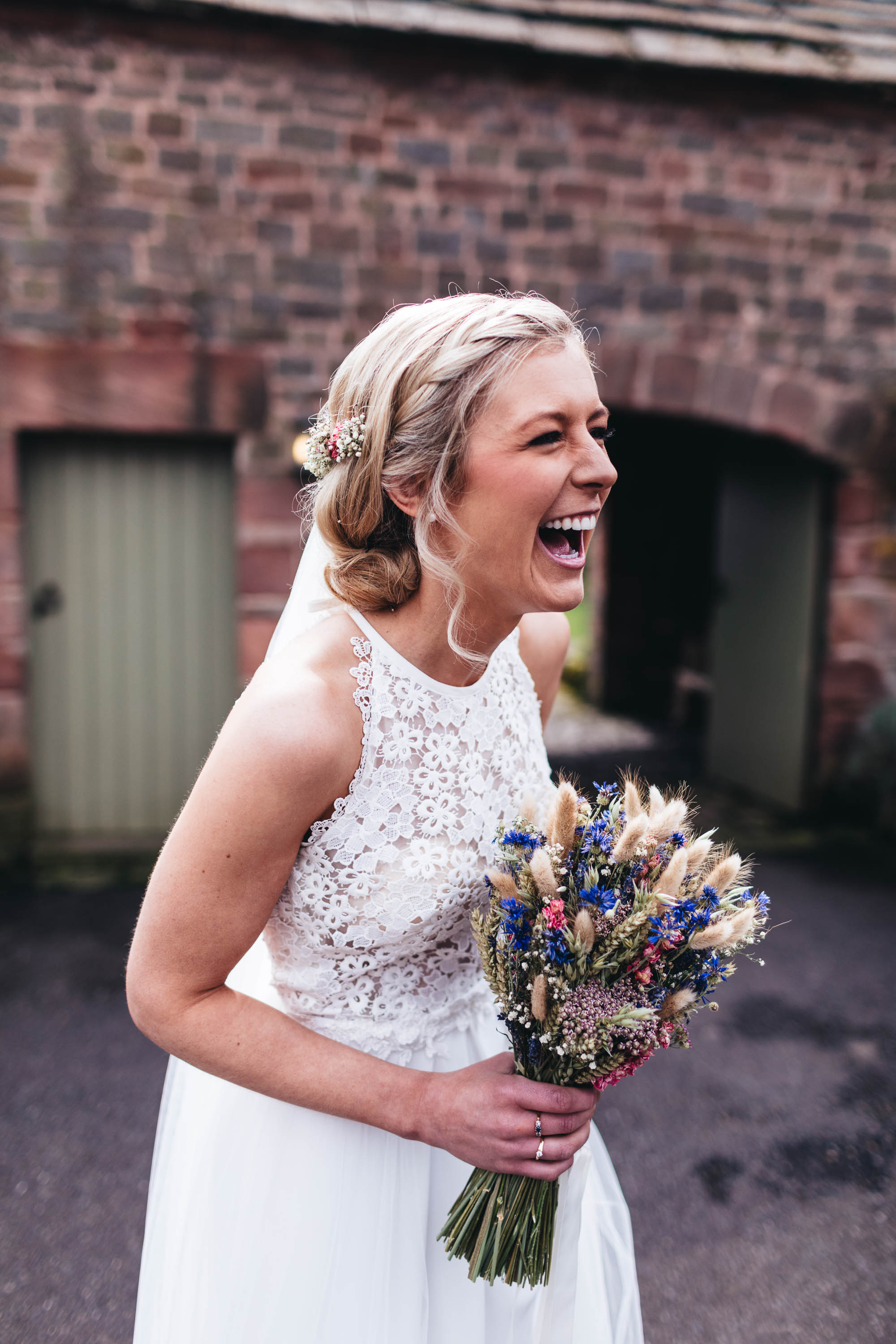 Bride laughs outside wedding barn venue holding dried flowers bouquet