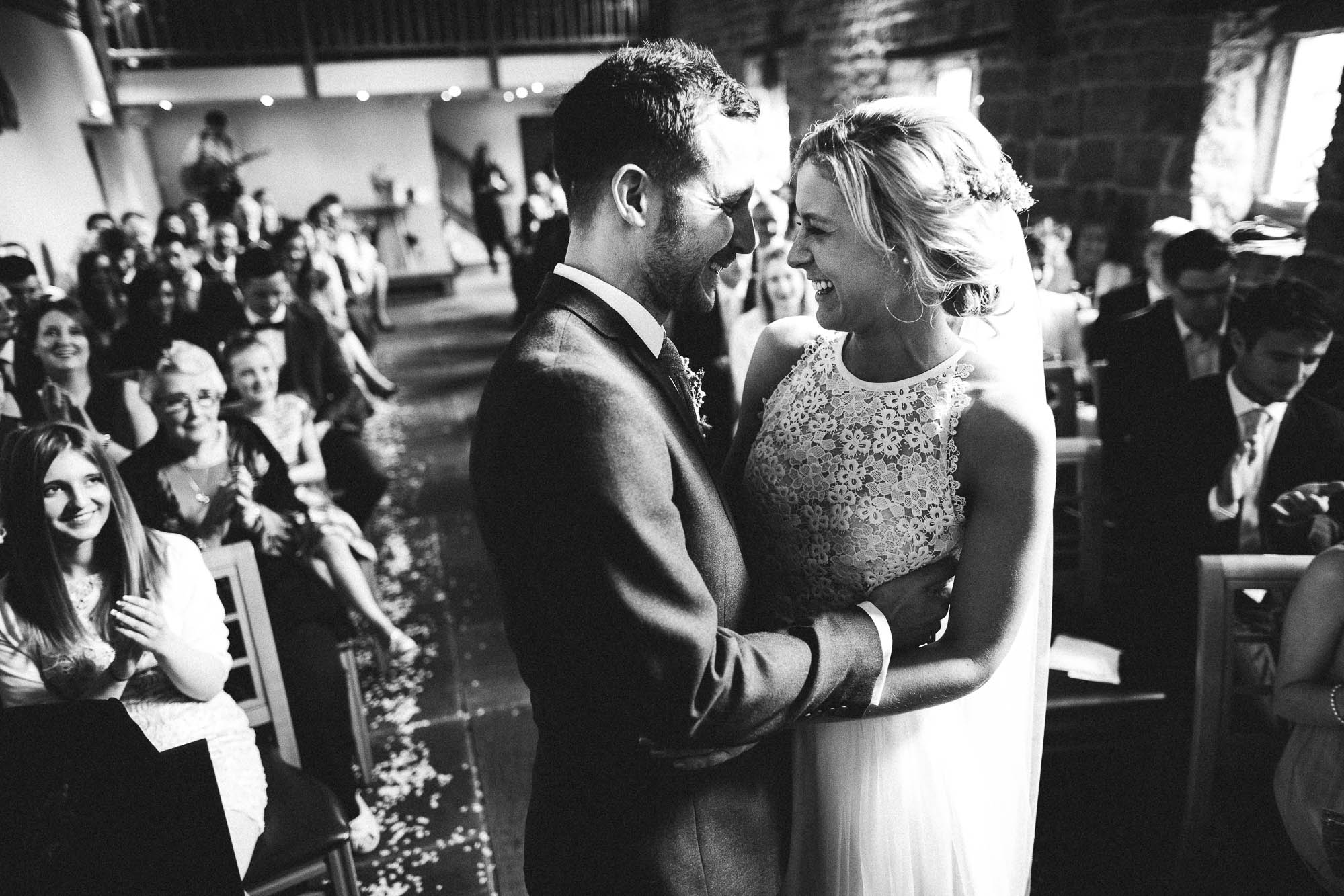 Monochrome shot of newlyweds embracing infront of wedding guests at The Ashes Wedding Barn