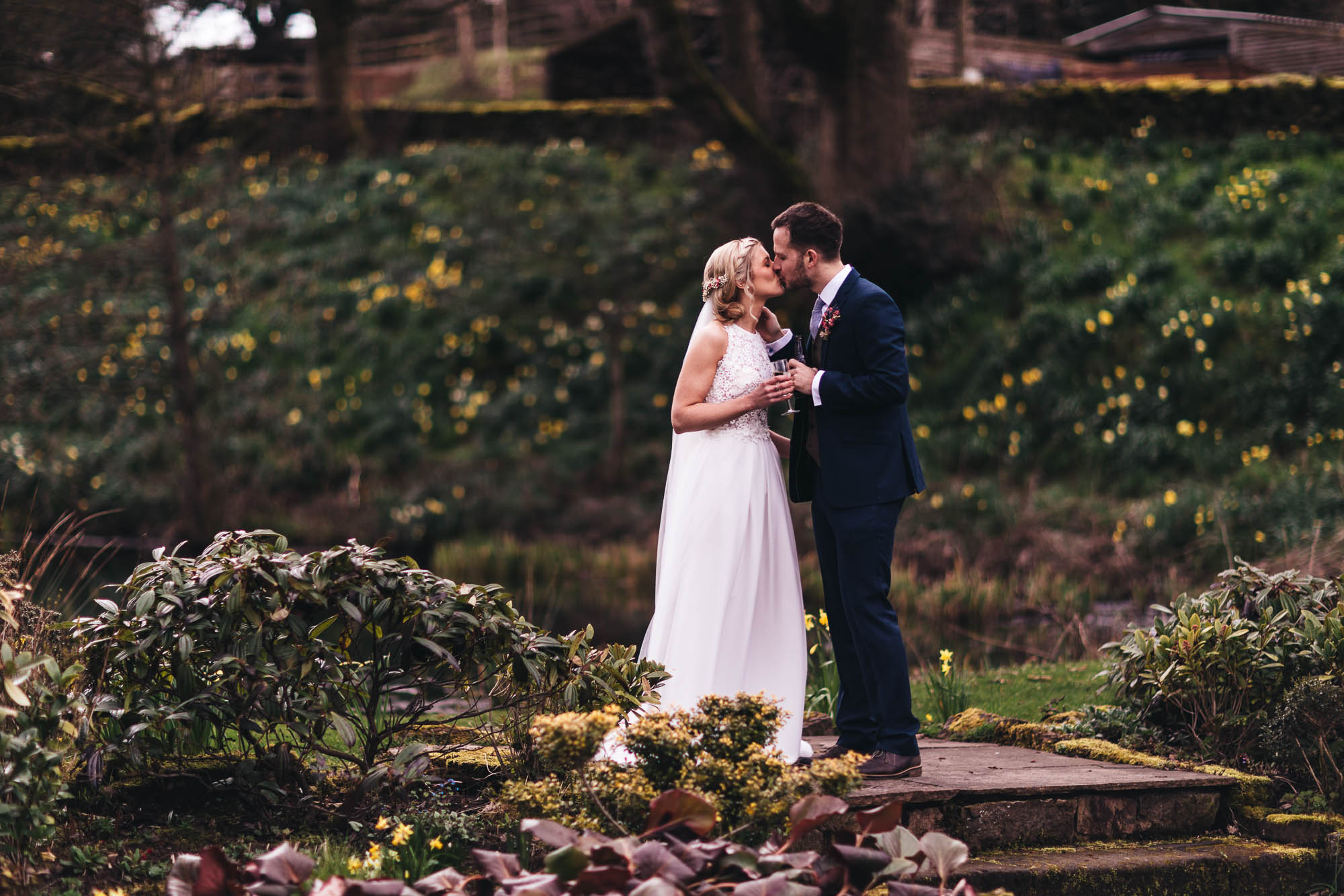 Newlyweds share a kiss and glass of bubbly surrounded by foliage