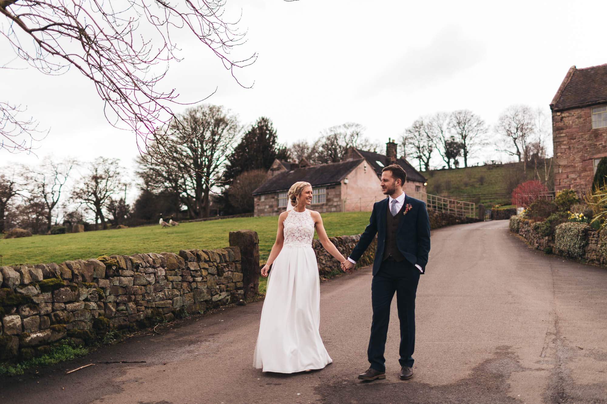 Bride and Groom hold hands and go for a wander after getting married with rustic barns in background