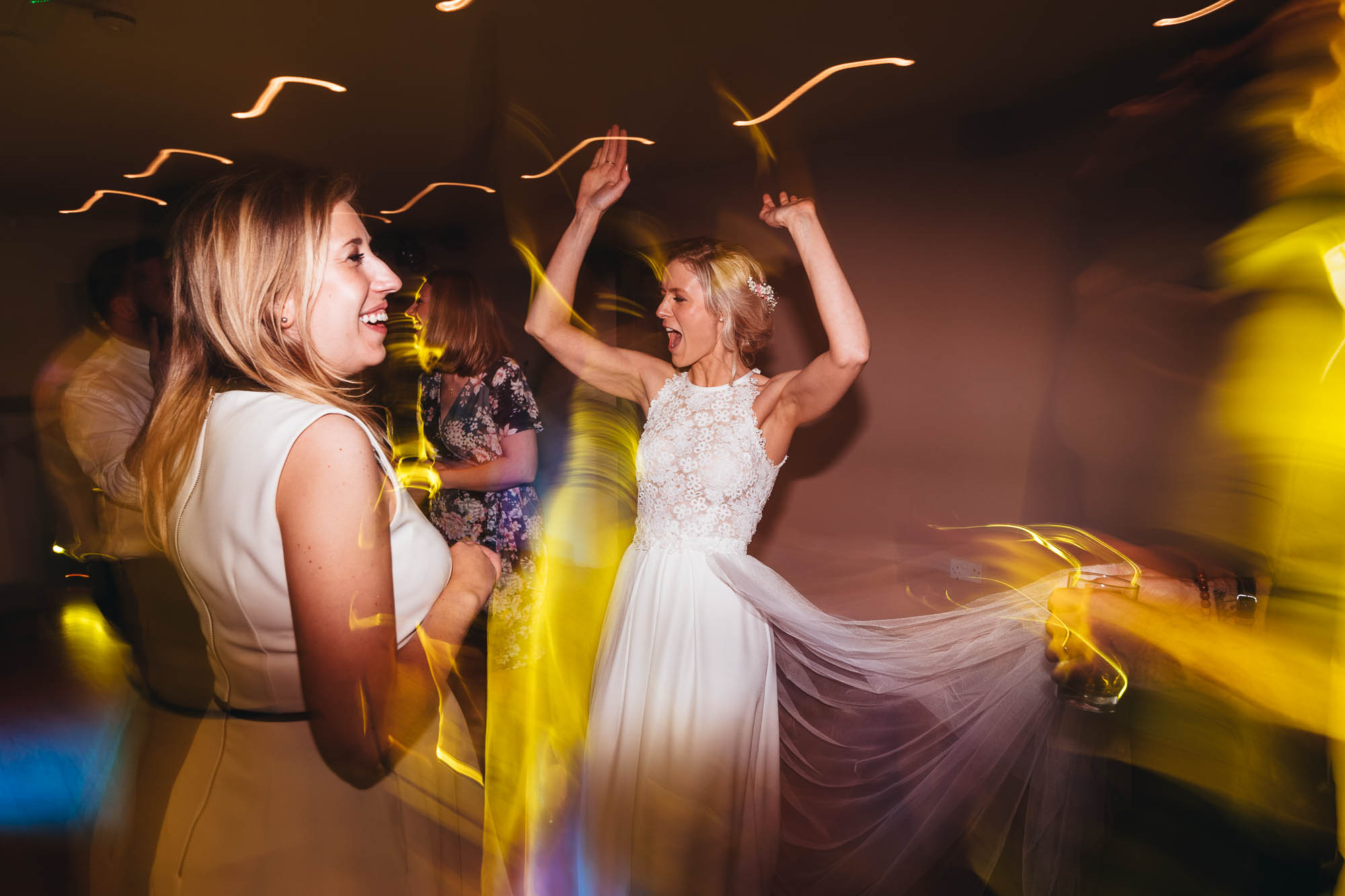 Bride raises her hands in the air and sings along on the dancefloor at wedding reception