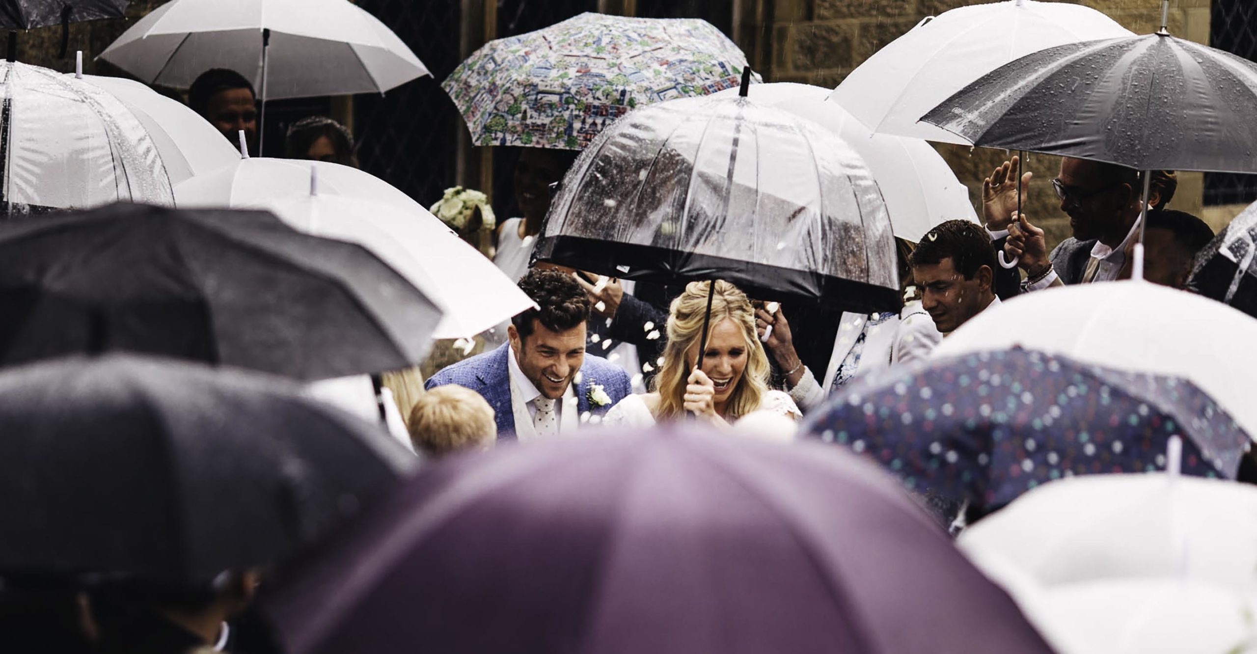 couple come out of church in the rain surrounded by umbrellas