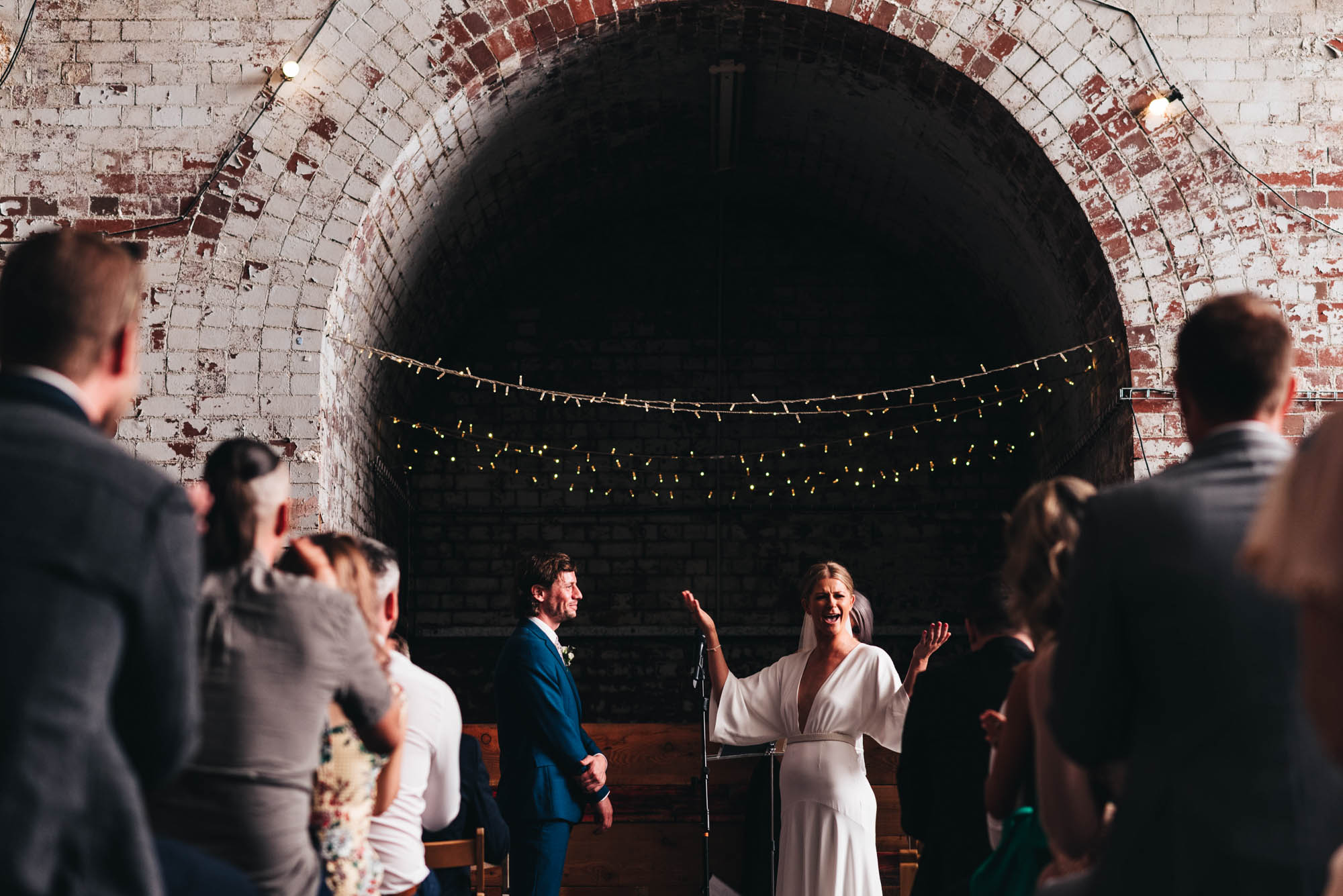 bride raises her hands with mouth open in expectation of a response from her guests