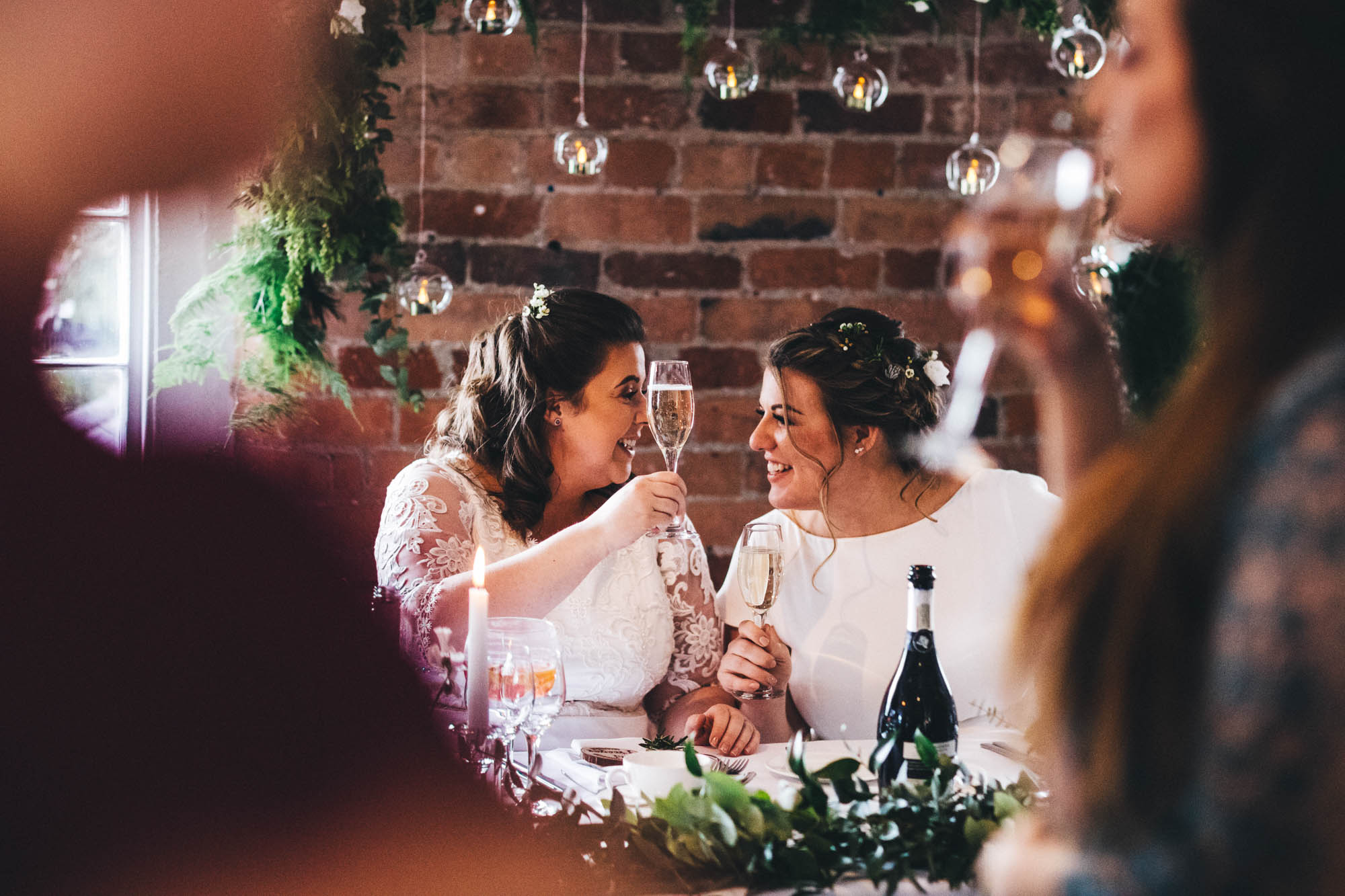 lesbian couple hold up their glasses in a gesture to say cheers on their wedding day