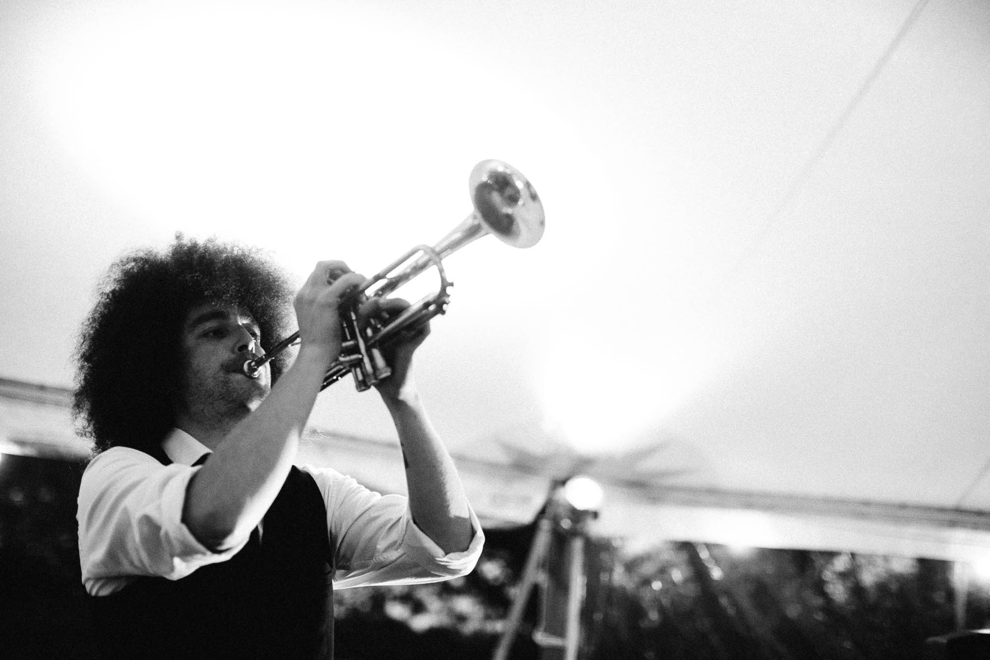 from the edge of the picture the trumpet player is in mid flow and has a very funky afro hair cut