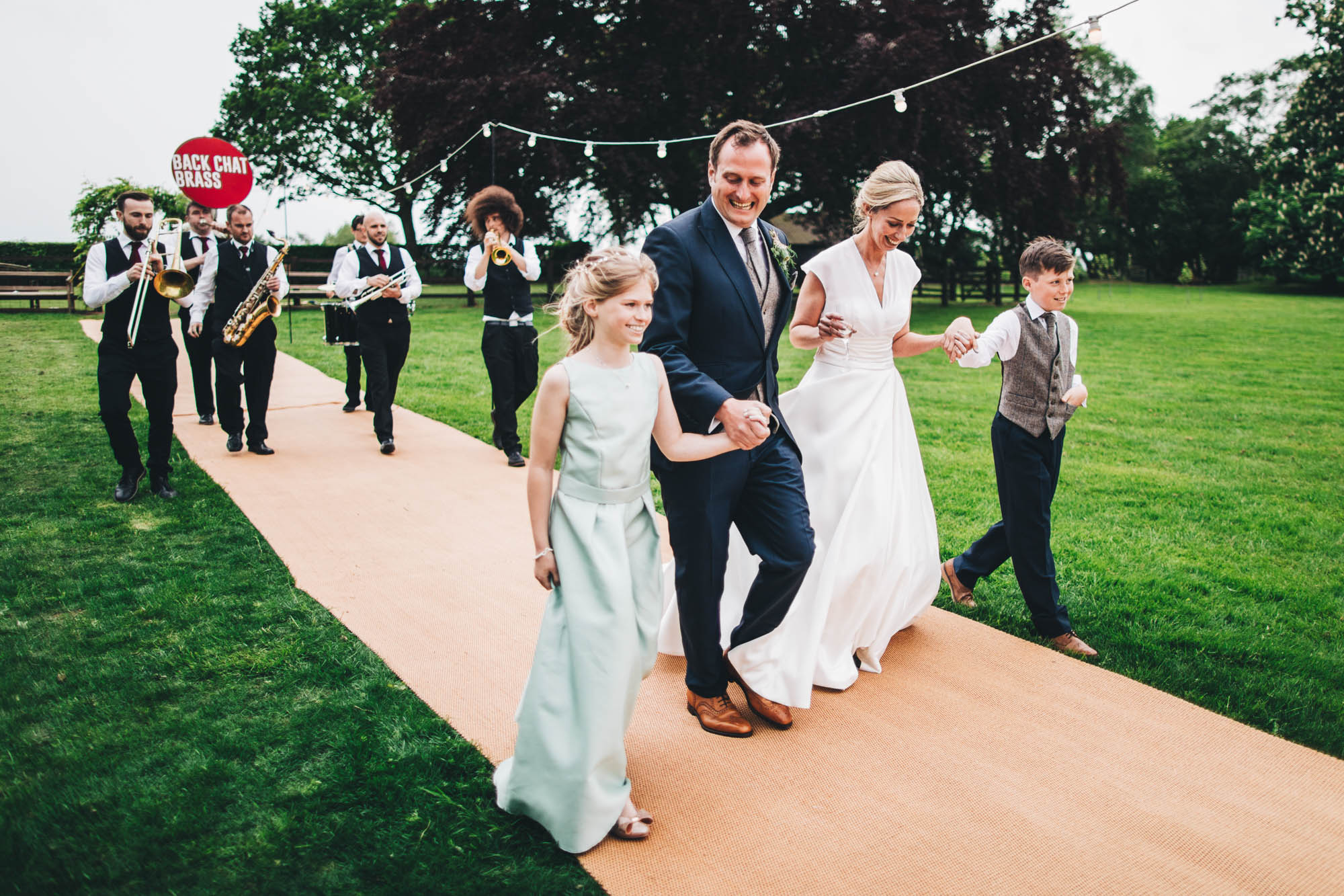 family enter the wedding reception marquee followed by a band
