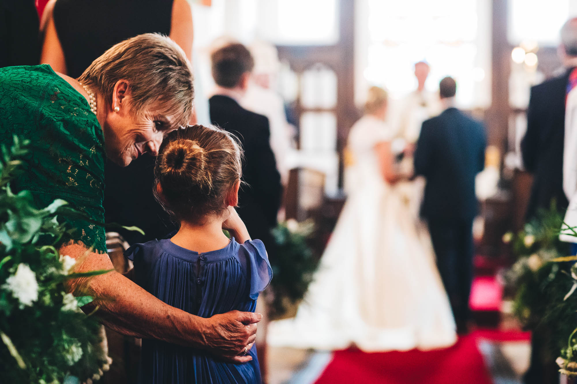 girl looks on at wedding ceremony as older lady hugs her