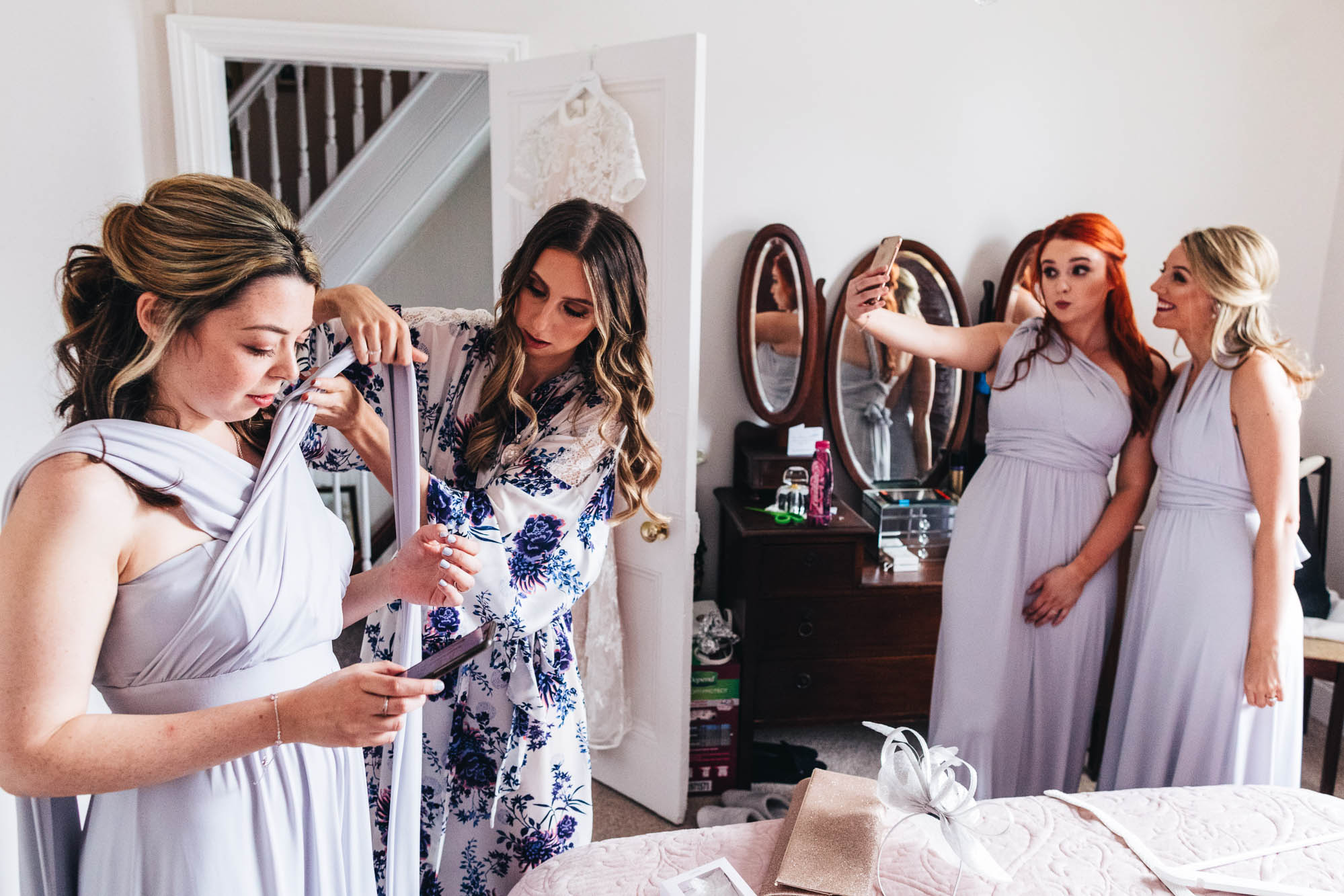 bride helps maid dress and other bridesmaids take a selfie in the background