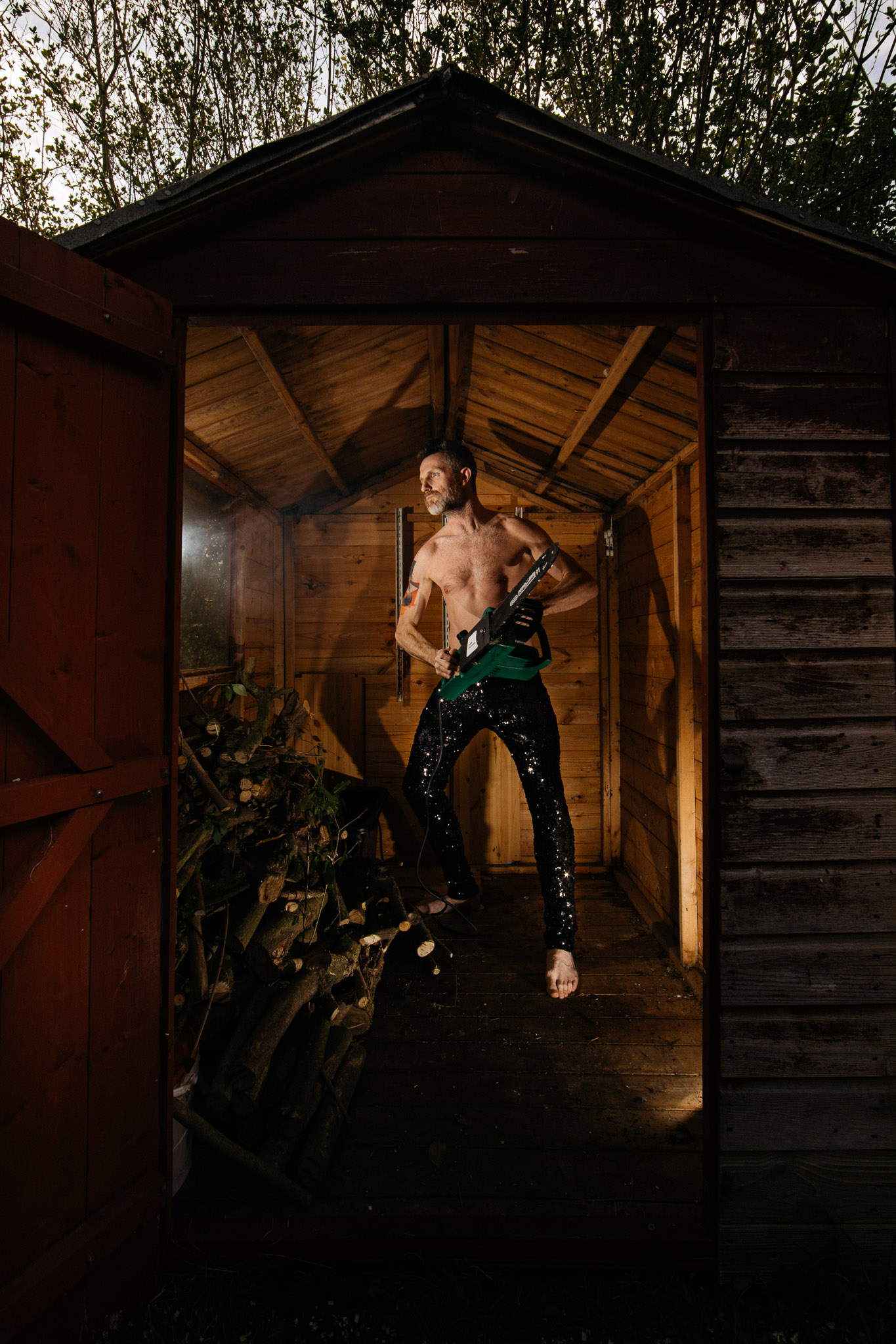 mike in shed with glitter trousers and chain saw