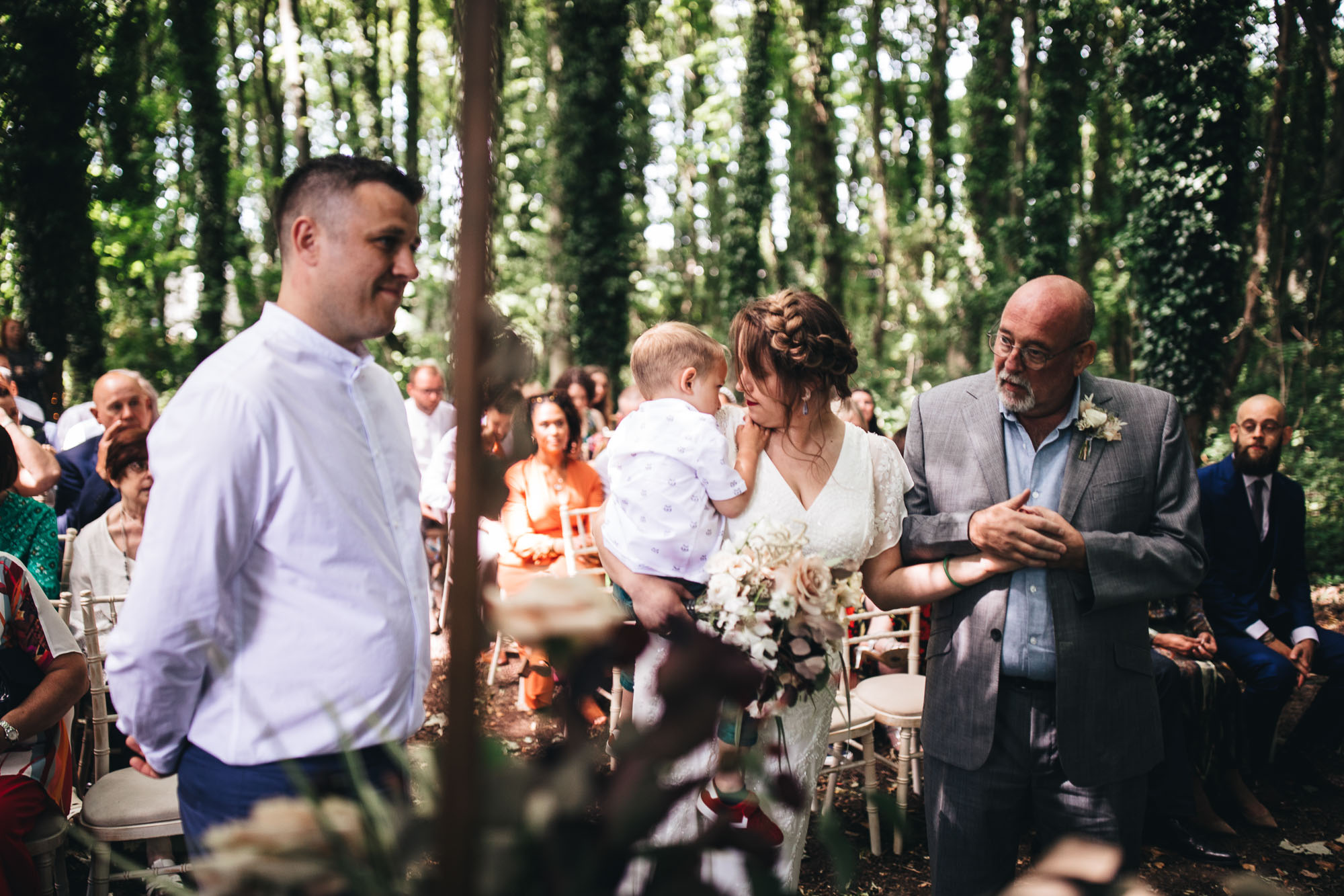 bride at front of ceremony with father and son in woodland