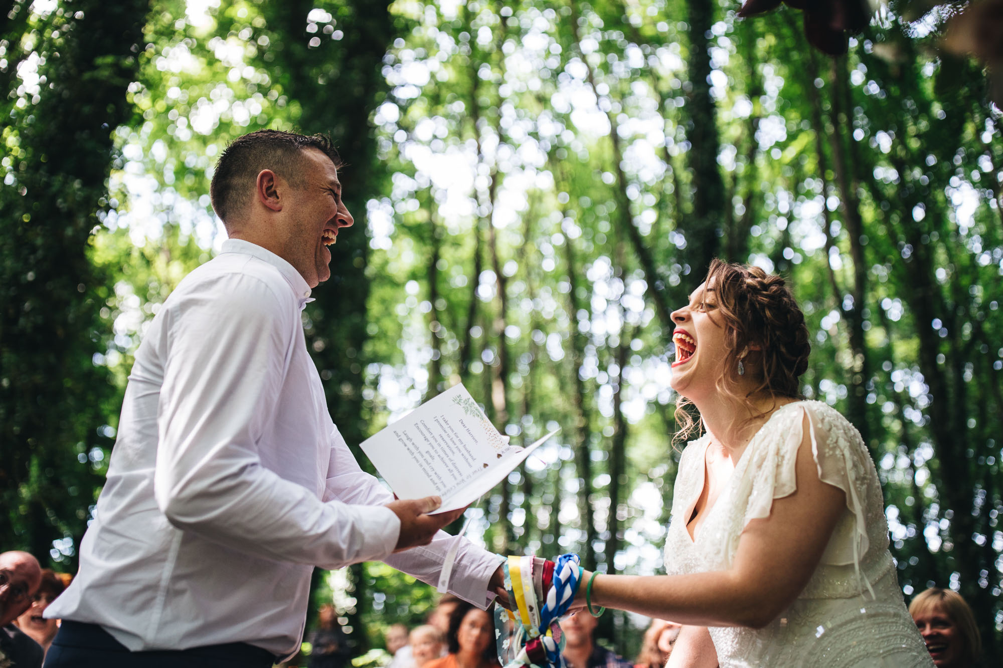 couple laugh at each other during the vows against the tree canopy backdrop