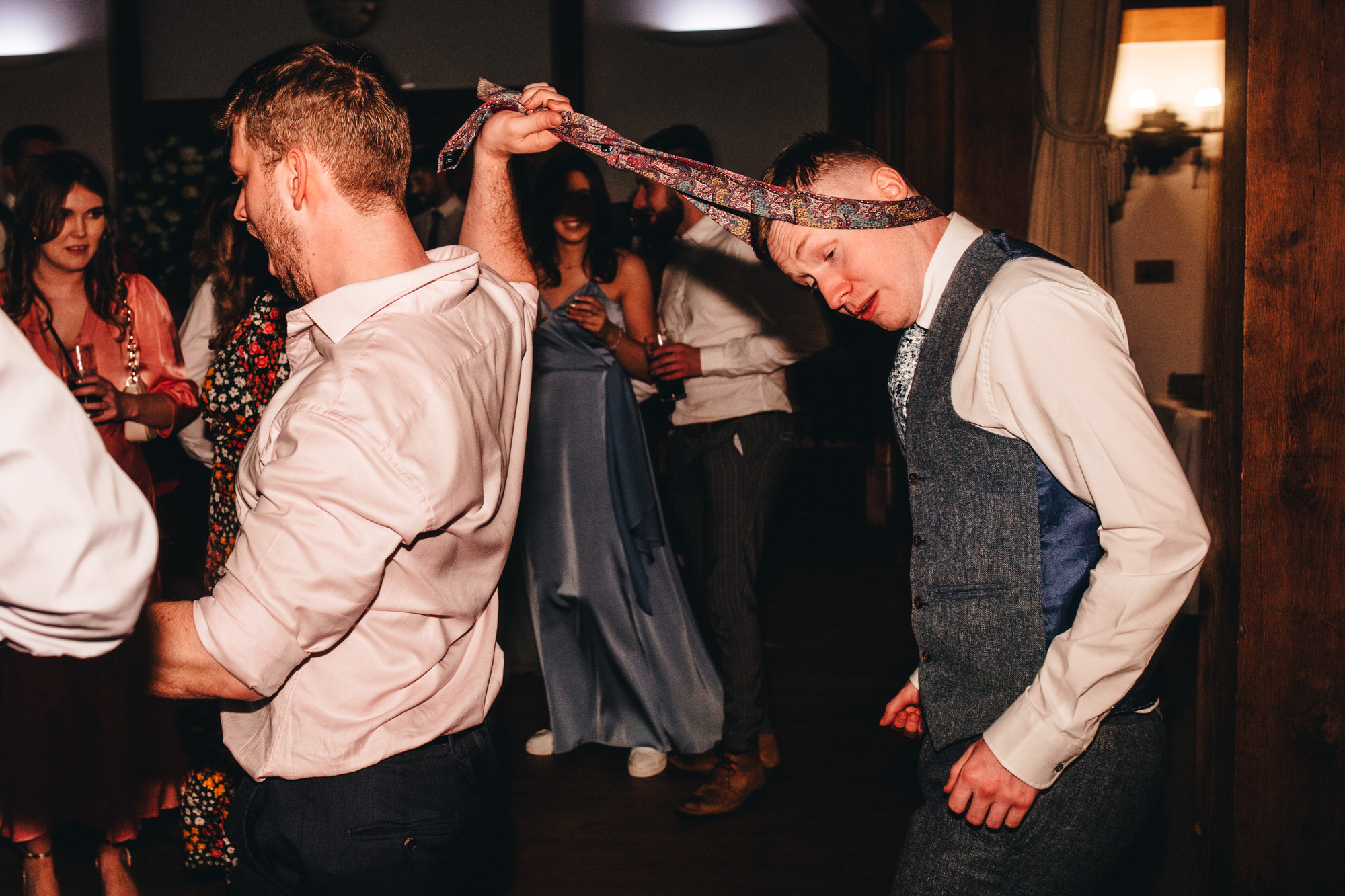 man leads another guest by his tie around his head onto the dancefloor