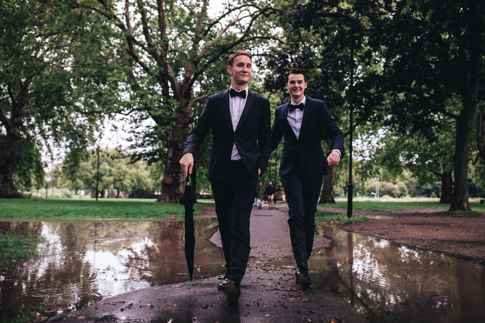 very smartly dressed dapper grooms walk over puddles